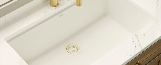 Ruvati 32" Undermount kitchen sink in arctic white with gold faucet and center drain on a white countertop.