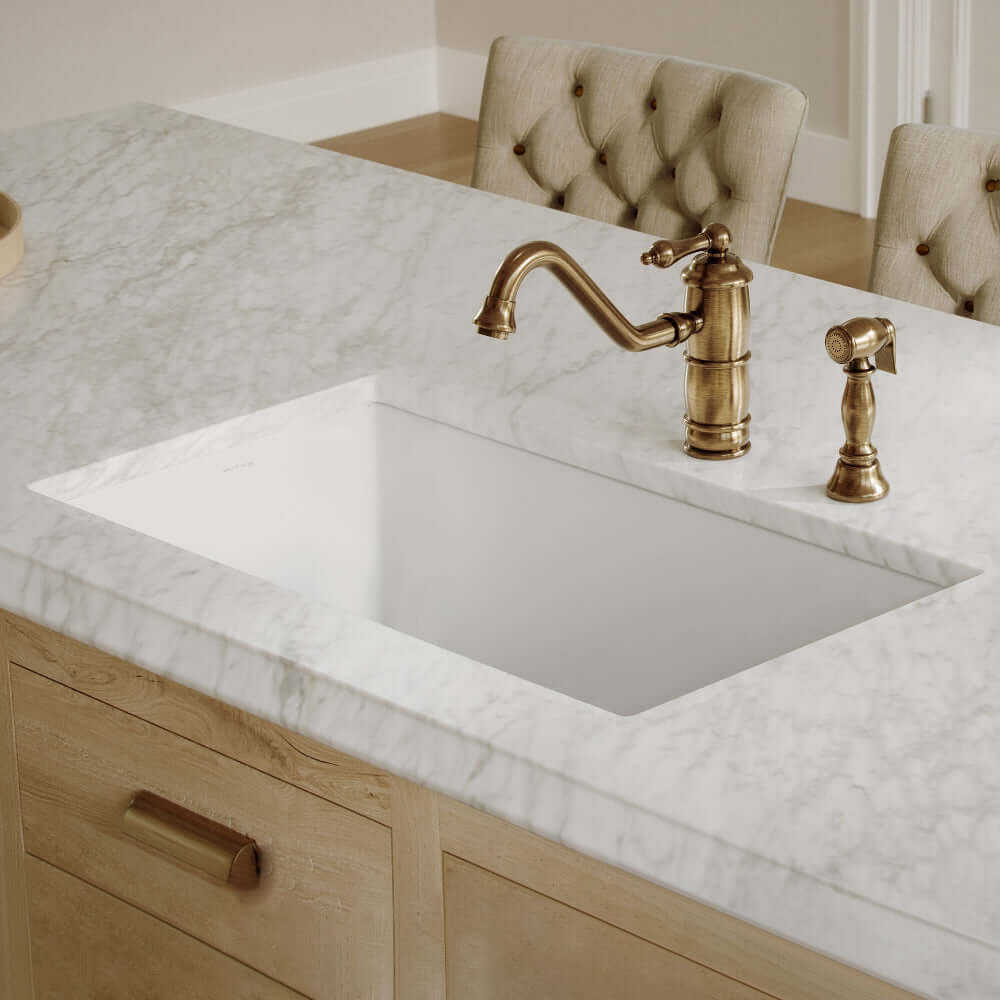 Whitehaus 34" dual mount fireclay sink with undermount installation in a marble-topped kitchen island with an antique brass faucet.