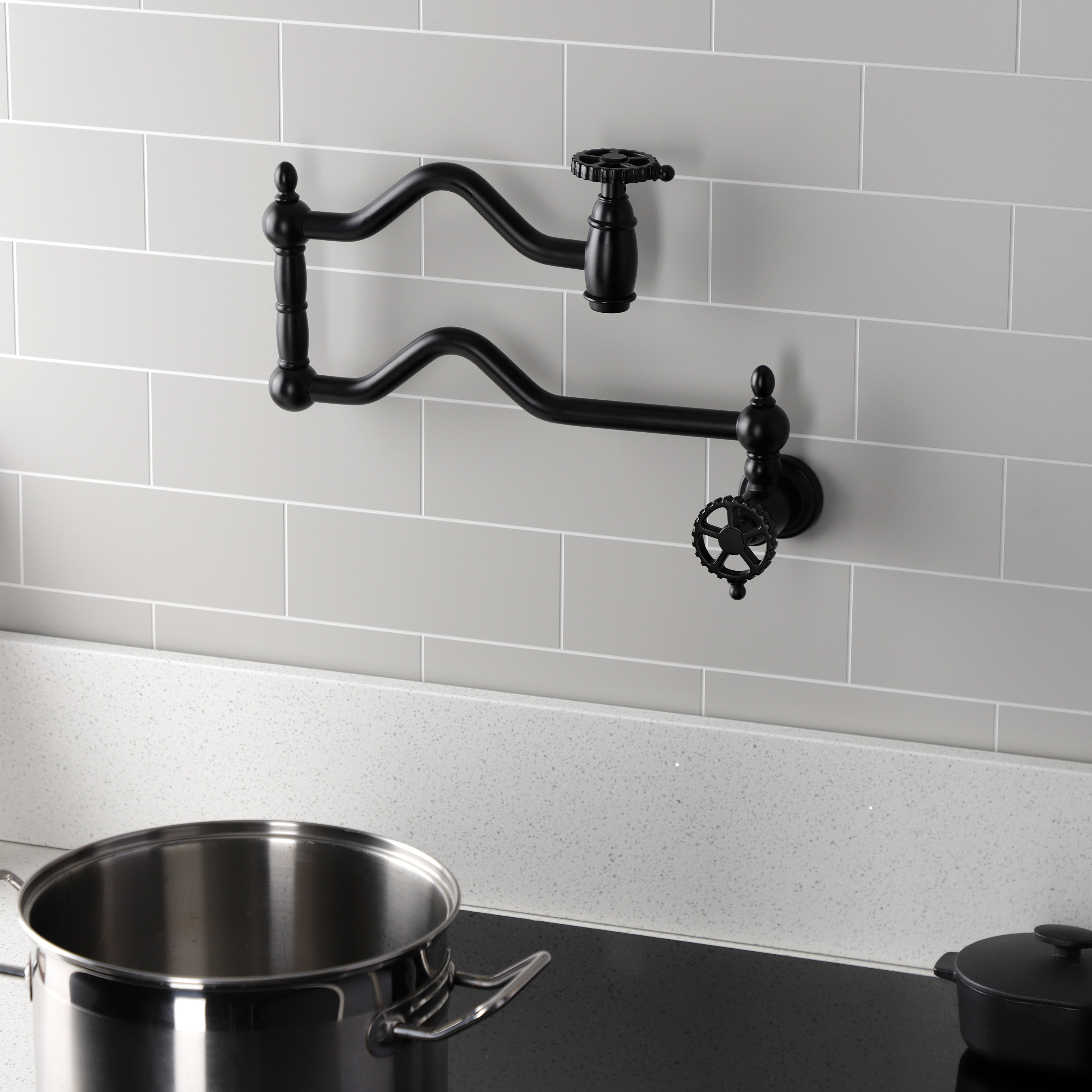 Kingston Brass KS2107CG Fuller Wall Mount Pot Filler Faucet, Brushed Brass against a gray tiled wall with a pot.