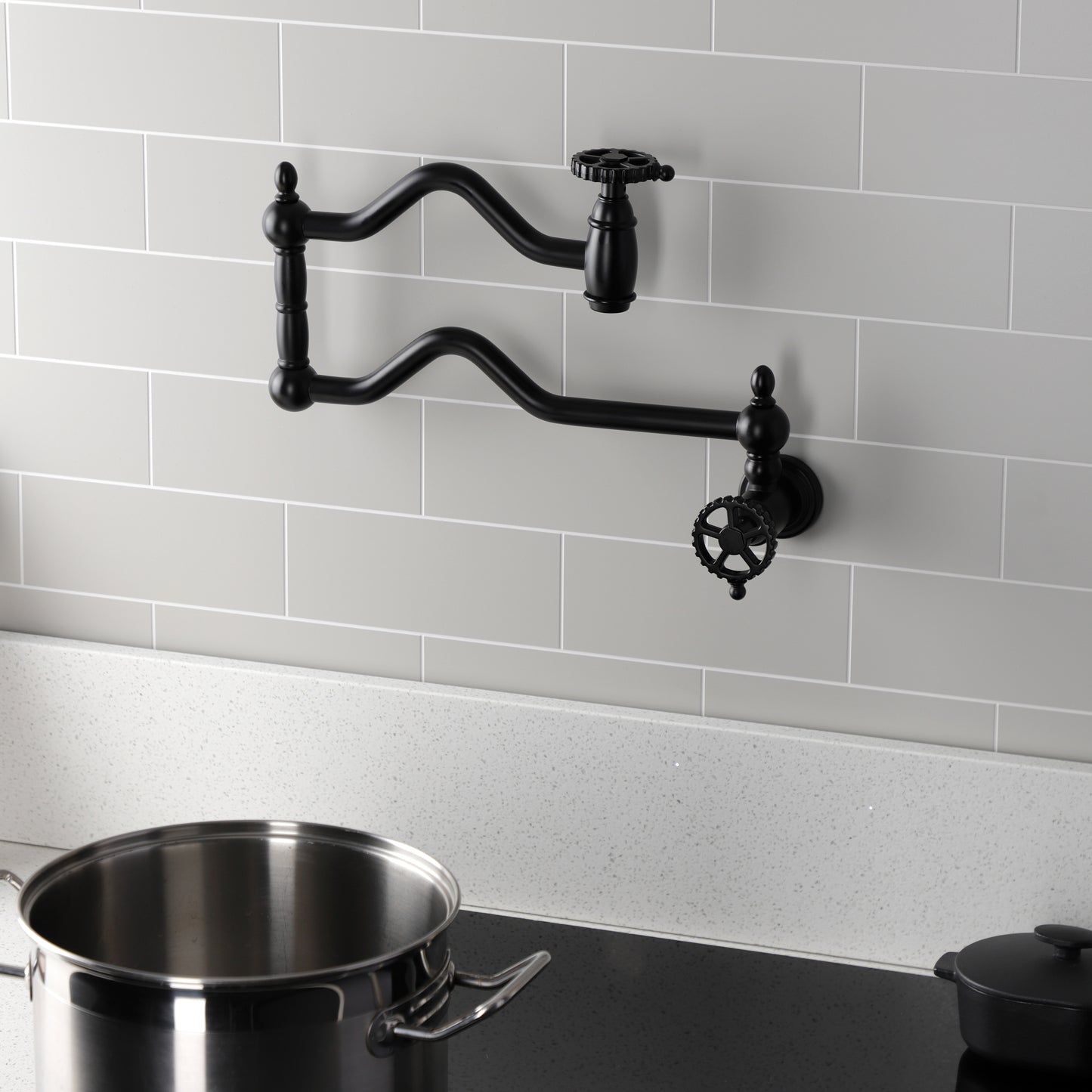 Kingston Brass KS2107CG Fuller Wall Mount Pot Filler Faucet, Brushed Brass against a gray tiled wall with a pot.