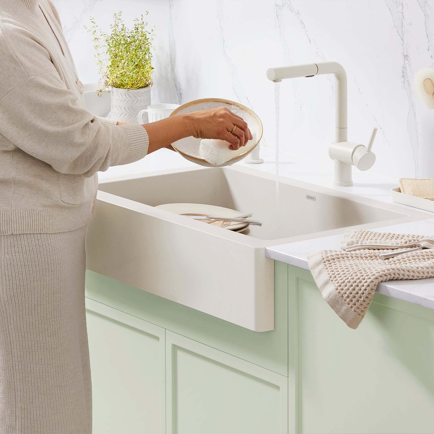 Woman using the BLANCO Linus Low Arc Pull-Out Dual-Spray Kitchen Faucet - Soft White in a modern kitchen sink.