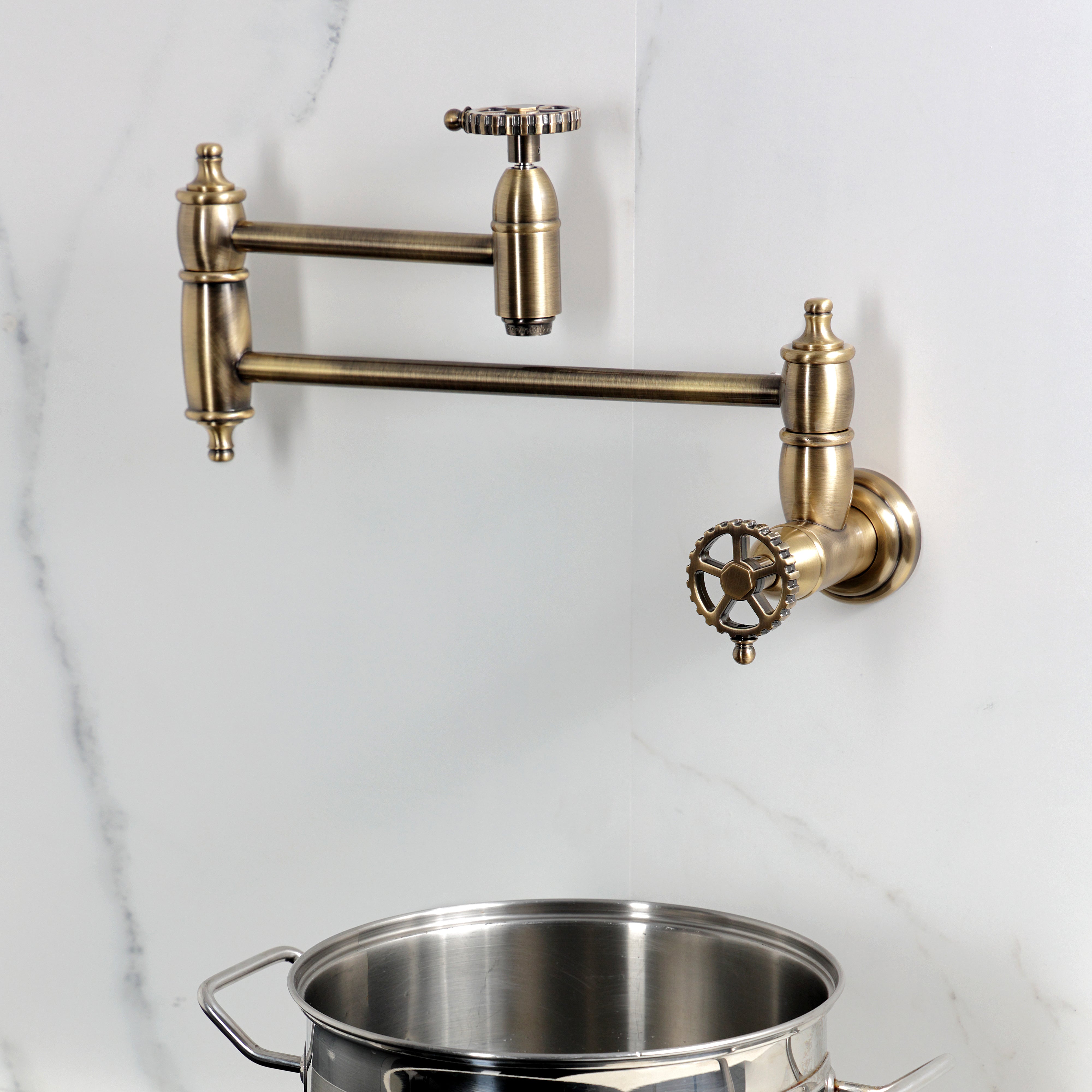 Kingston Brass KS3103CG Fuller Wall Mount Pot Filler Faucet, Antique Brass with a pot underneath.
