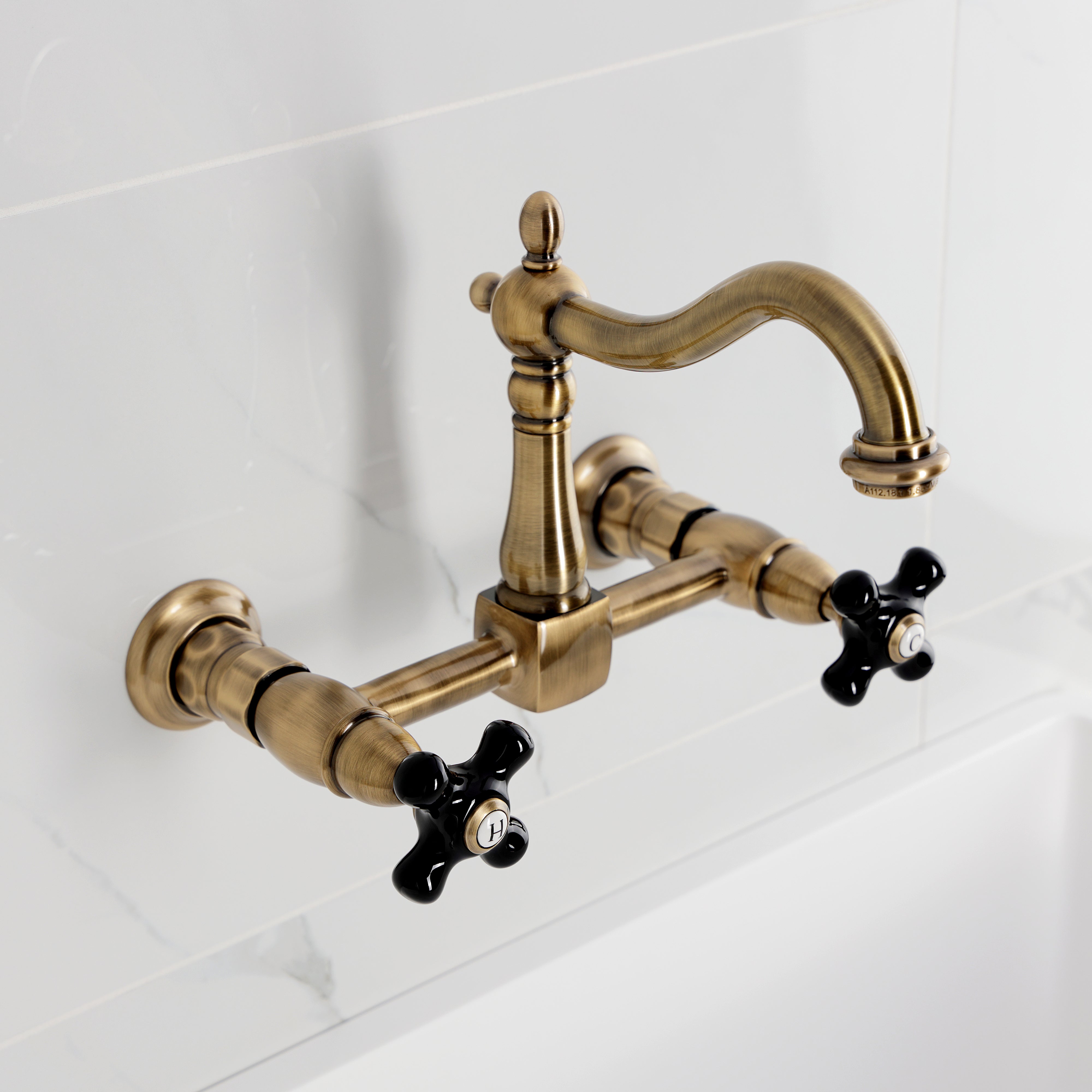 Kingston KS1263PKX Duchess Two-Handle Wall Mount Bridge Kitchen Faucet, Antique Brass with black porcelain handles.