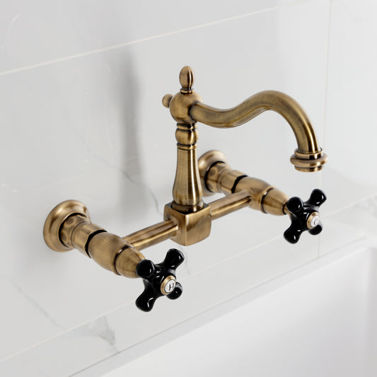 Kingston KS1263PKX Duchess Two-Handle Wall Mount Bridge Kitchen Faucet, Antique Brass with black porcelain handles.