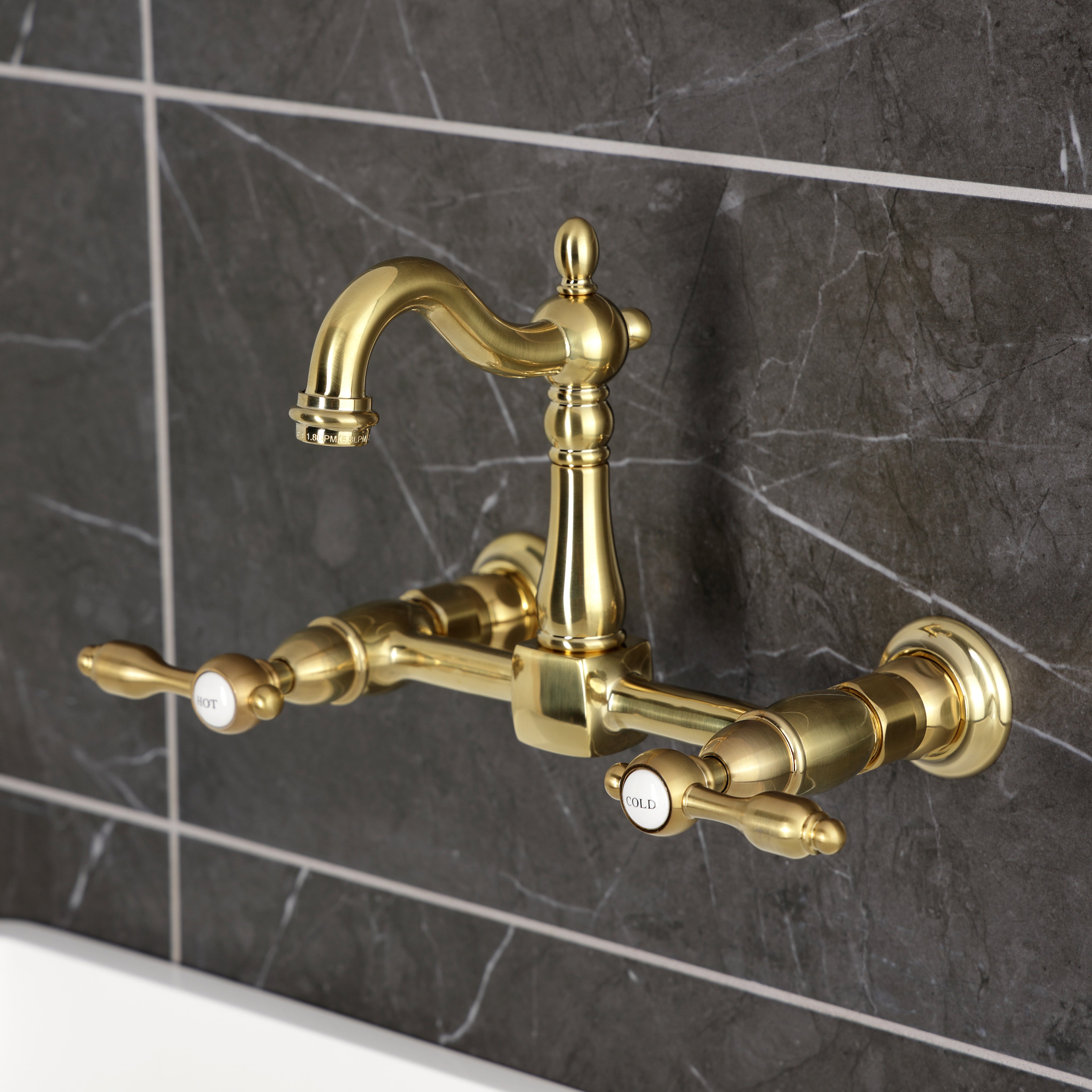 Kingston KS2443TAL Tudor Two-Handle Wall Mount Bridge Kitchen Faucet, Antique Brass on dark tile background.