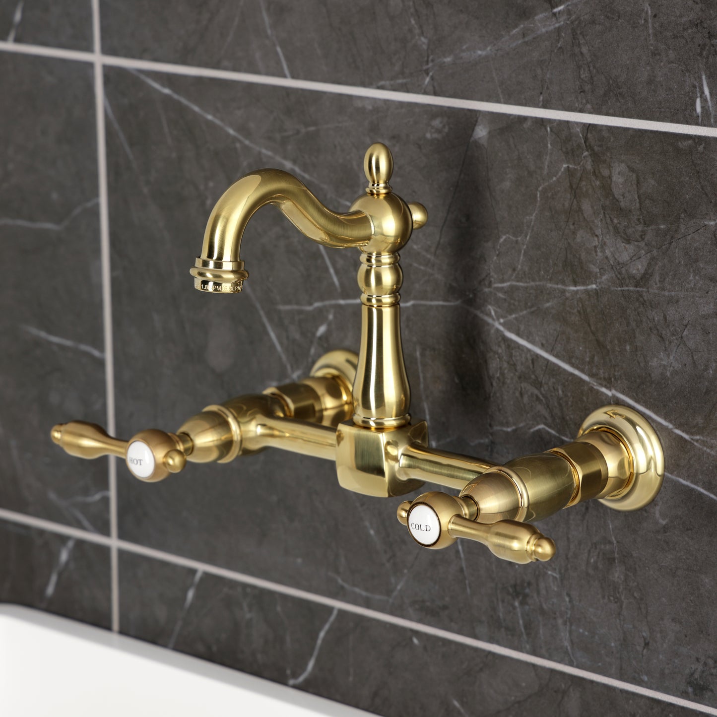 Kingston KS2443TAL Tudor Two-Handle Wall Mount Bridge Kitchen Faucet, Antique Brass on dark tile background.