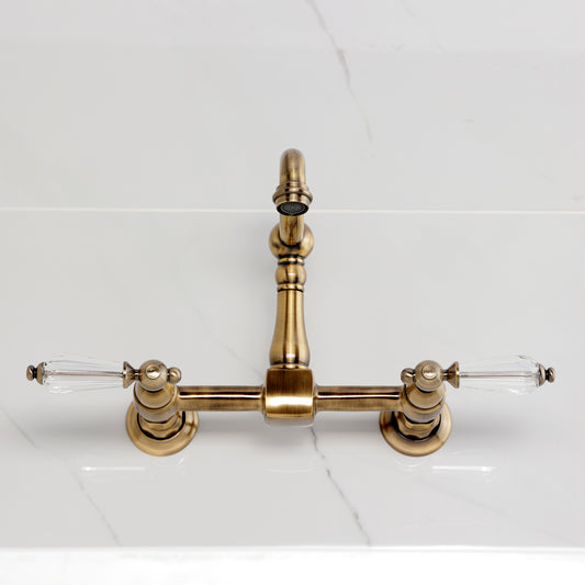 Kingston KS2443WLL Willshire Two-Handle Wall Mount Bridge Kitchen Faucet, Antique Brass on marble countertop.