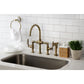 Kingston KS2333KL Whitaker Industrial Style Bridge Kitchen Faucet with Brass Sprayer, Antique Brass in modern kitchen setting.