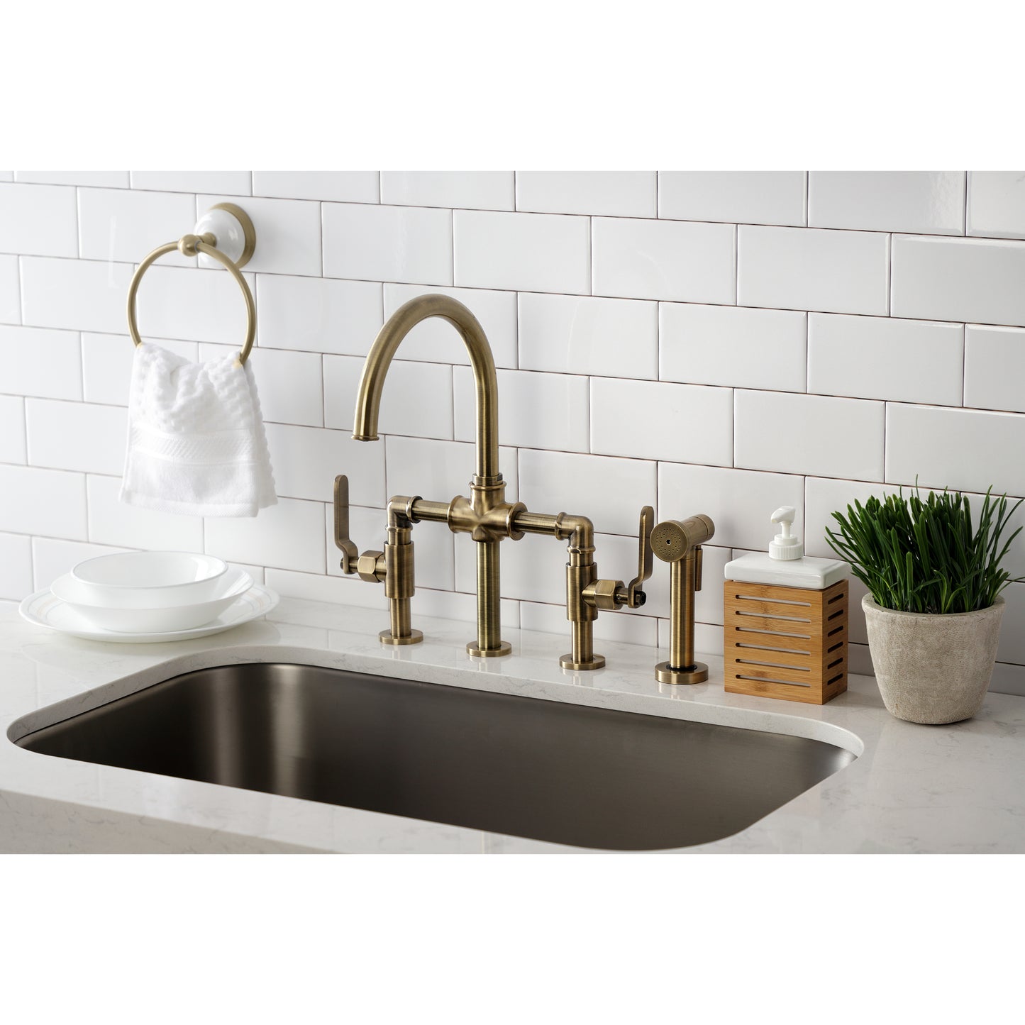 Kingston KS2333KL Whitaker Industrial Style Bridge Kitchen Faucet with Brass Sprayer, Antique Brass in modern kitchen setting.