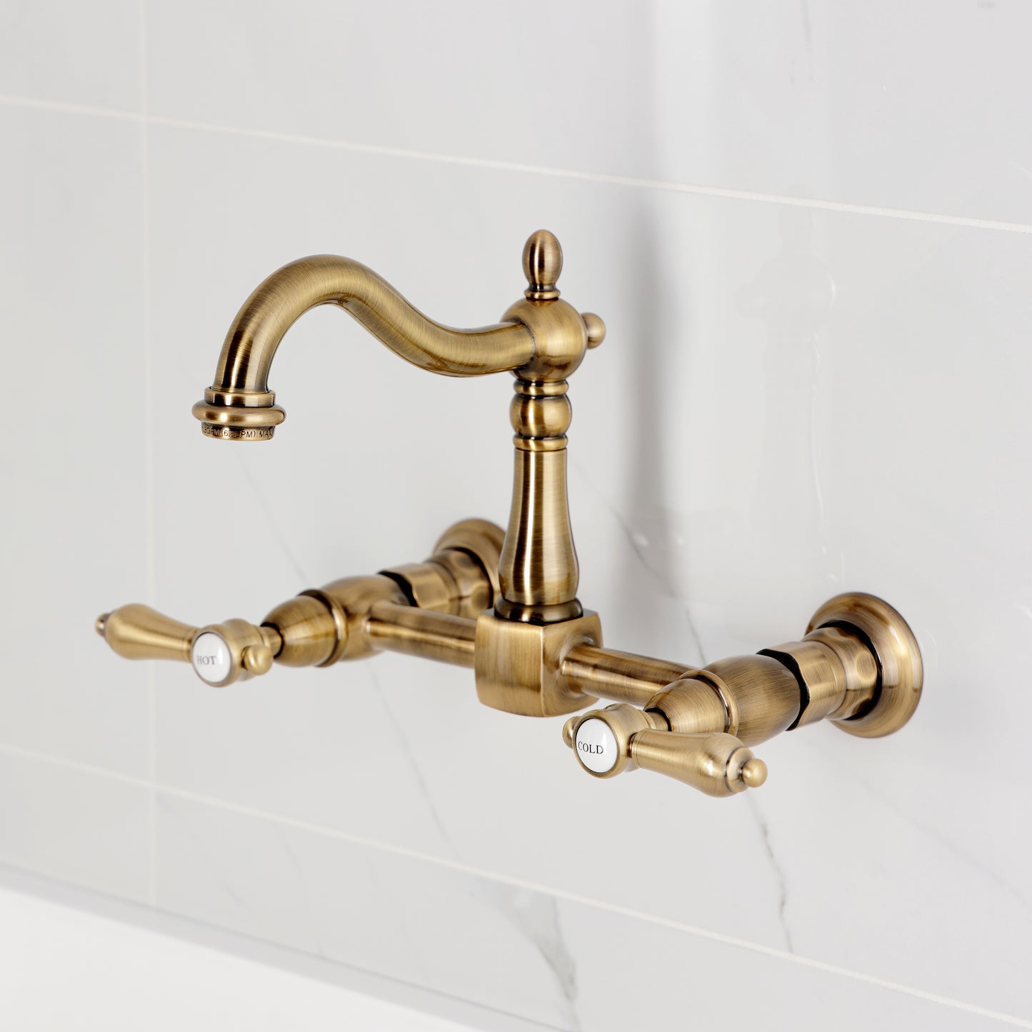 Kingston KS1263BAL Heirloom Two-Handle Wall Mount Bridge Kitchen Faucet, Antique Brass on a white tile background.