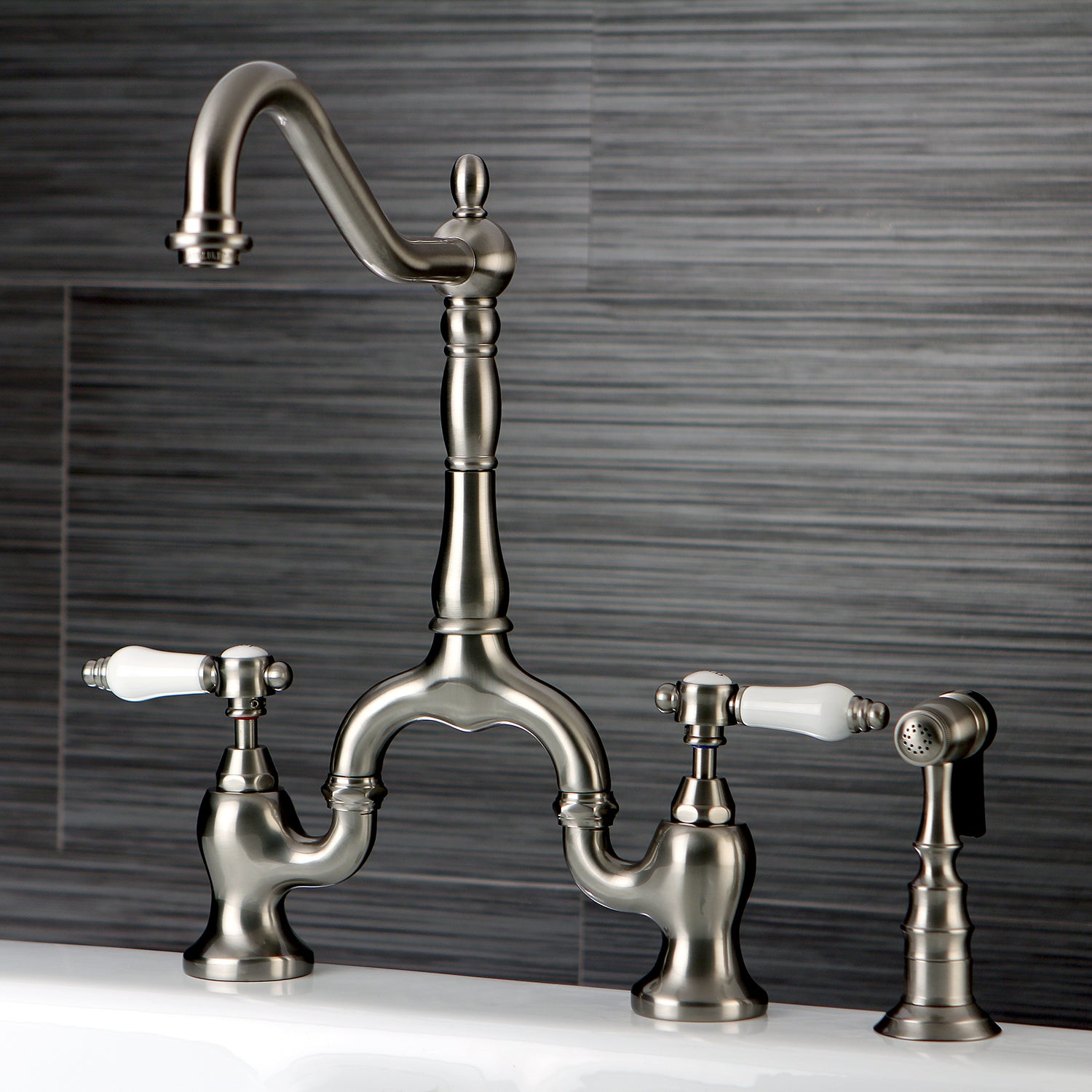 Kingston KS7753BPLBS Bel-Air Bridge Kitchen Faucet with Brass Sprayer, Antique Brass in a sleek design with porcelain levers.