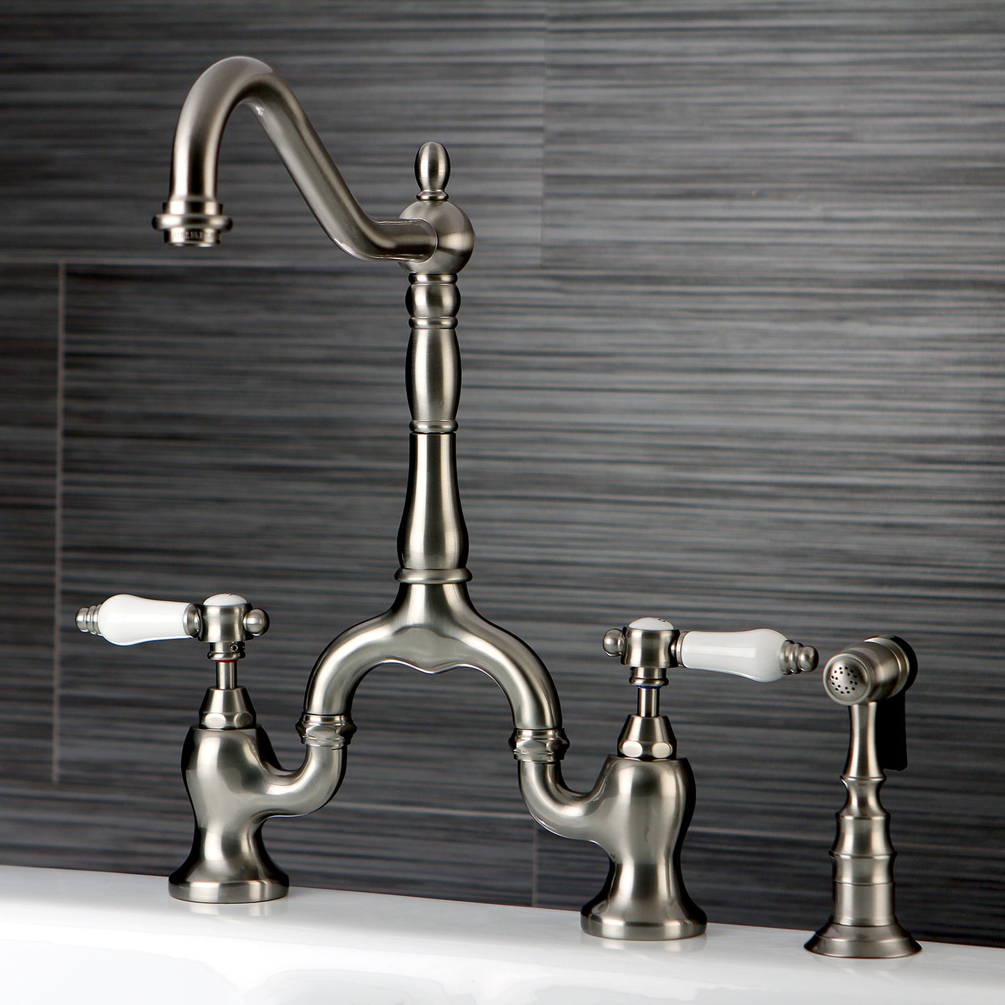 Kingston KS7753BPLBS Bel-Air Bridge Kitchen Faucet with Brass Sprayer, Antique Brass in a sleek design with porcelain levers.