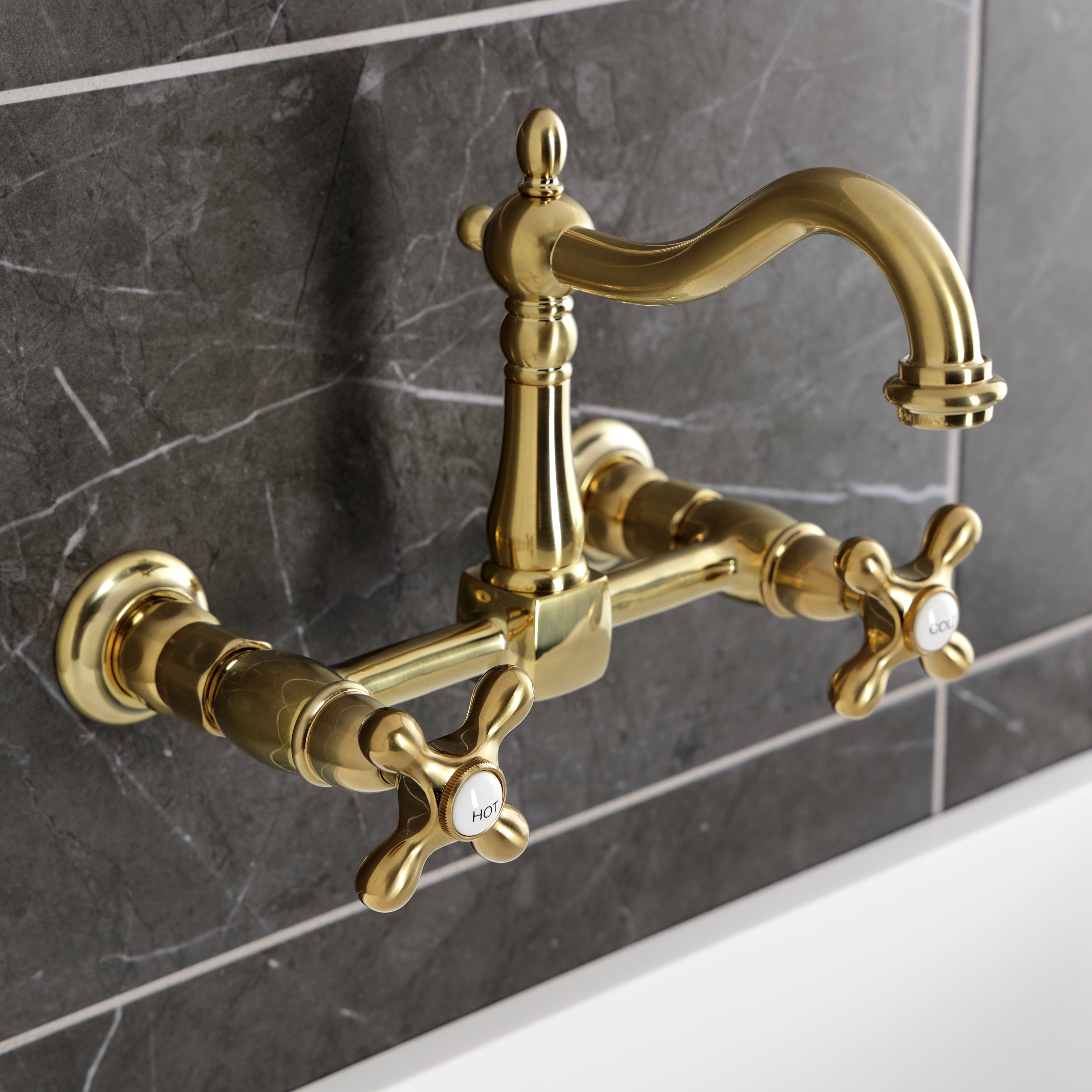 Kingston KS1263AX Heritage Two-Handle Wall Mount Bridge Kitchen Faucet, Antique Brass against a dark tiled background.