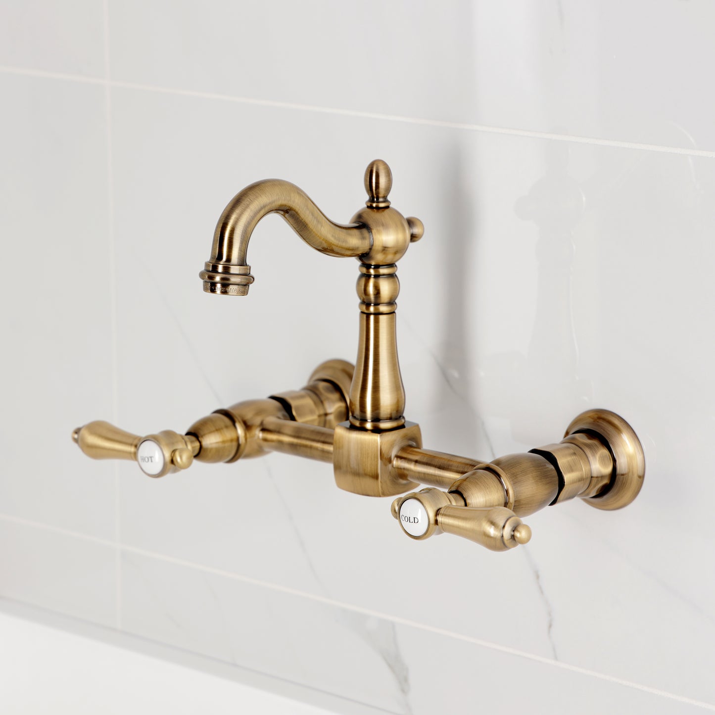 Kingston KS2443BAL Heirloom Two-Handle Wall Mount Bridge Kitchen Faucet, Antique Brass showing hot and cold handles.