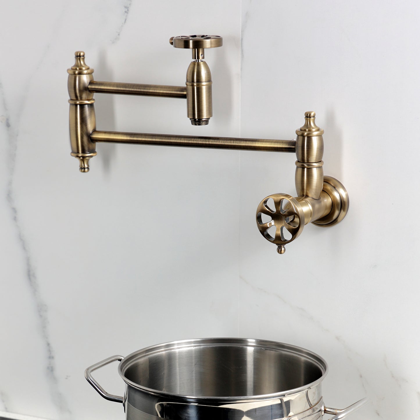 Kingston Brass KS3103RX Belknap Wall Mount Pot Filler Faucet, Antique Brass on a wall with a stainless steel pot below.