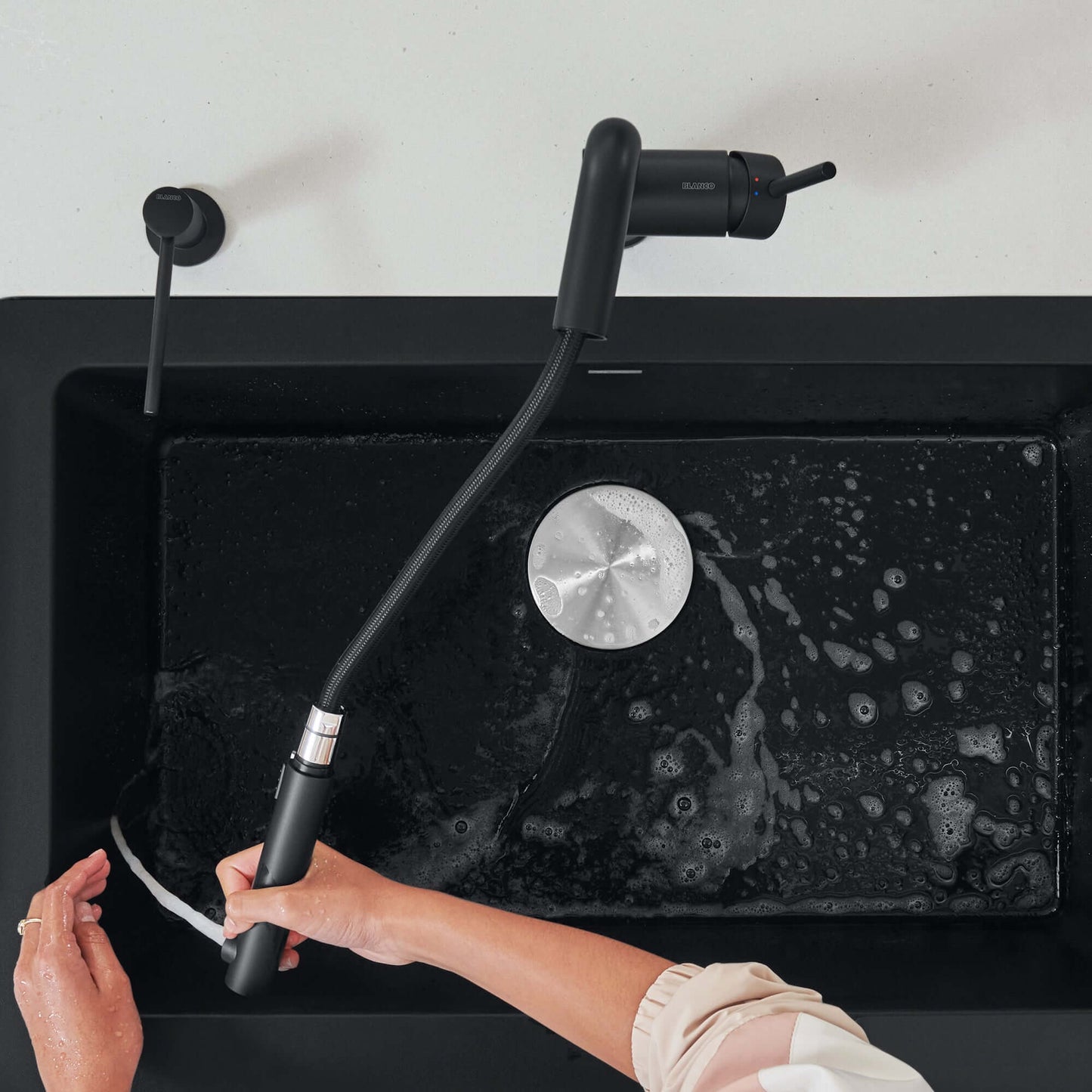 BLANCO Linus Low Arc Pull-Out Dual-Spray Kitchen Faucet - in use over a black sink with water flowing.