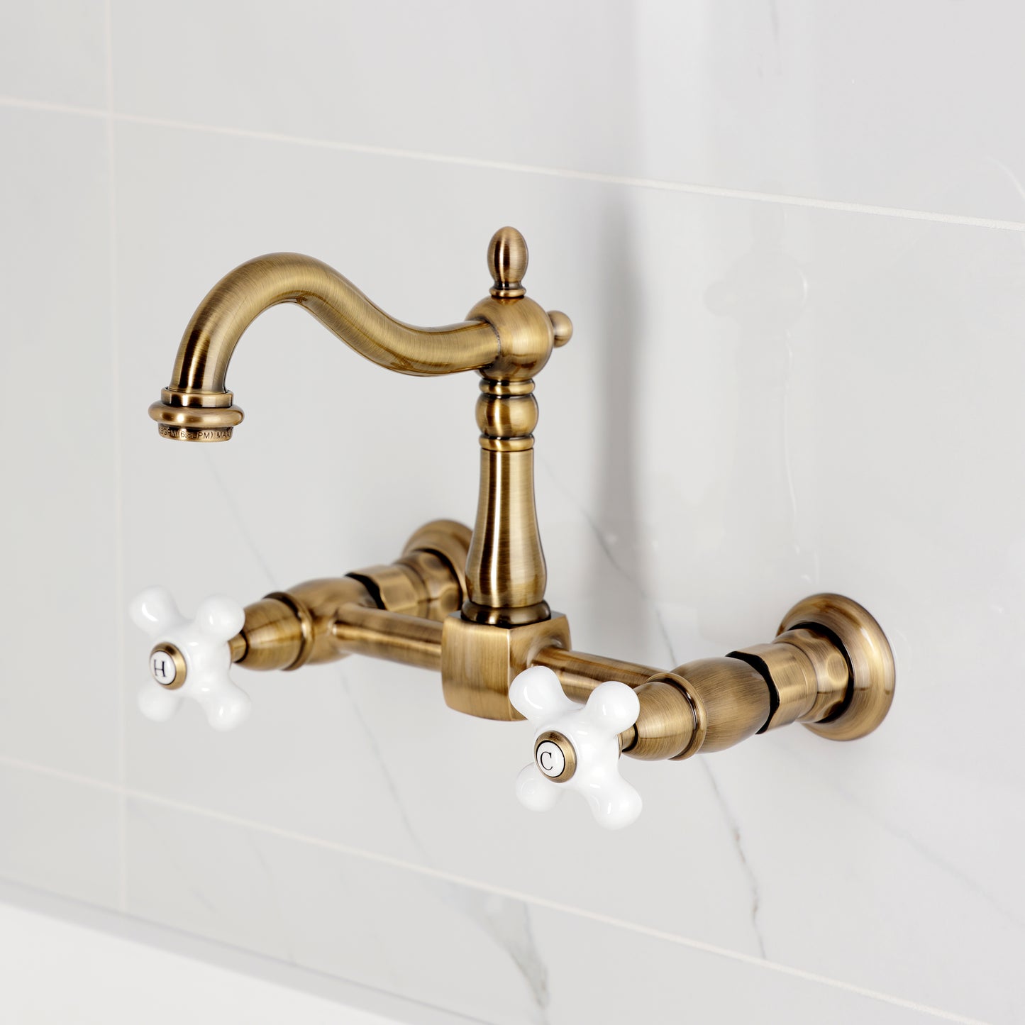 Kingston KS1263PX Heritage Two-Handle Wall Mount Bridge Kitchen Faucet, Antique Brass on a white tiled background.