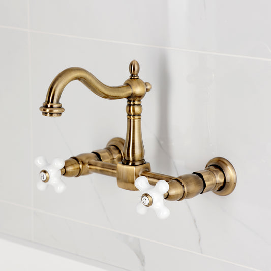 Kingston KS1263PX Heritage Two-Handle Wall Mount Bridge Kitchen Faucet, Antique Brass on a white tiled background.
