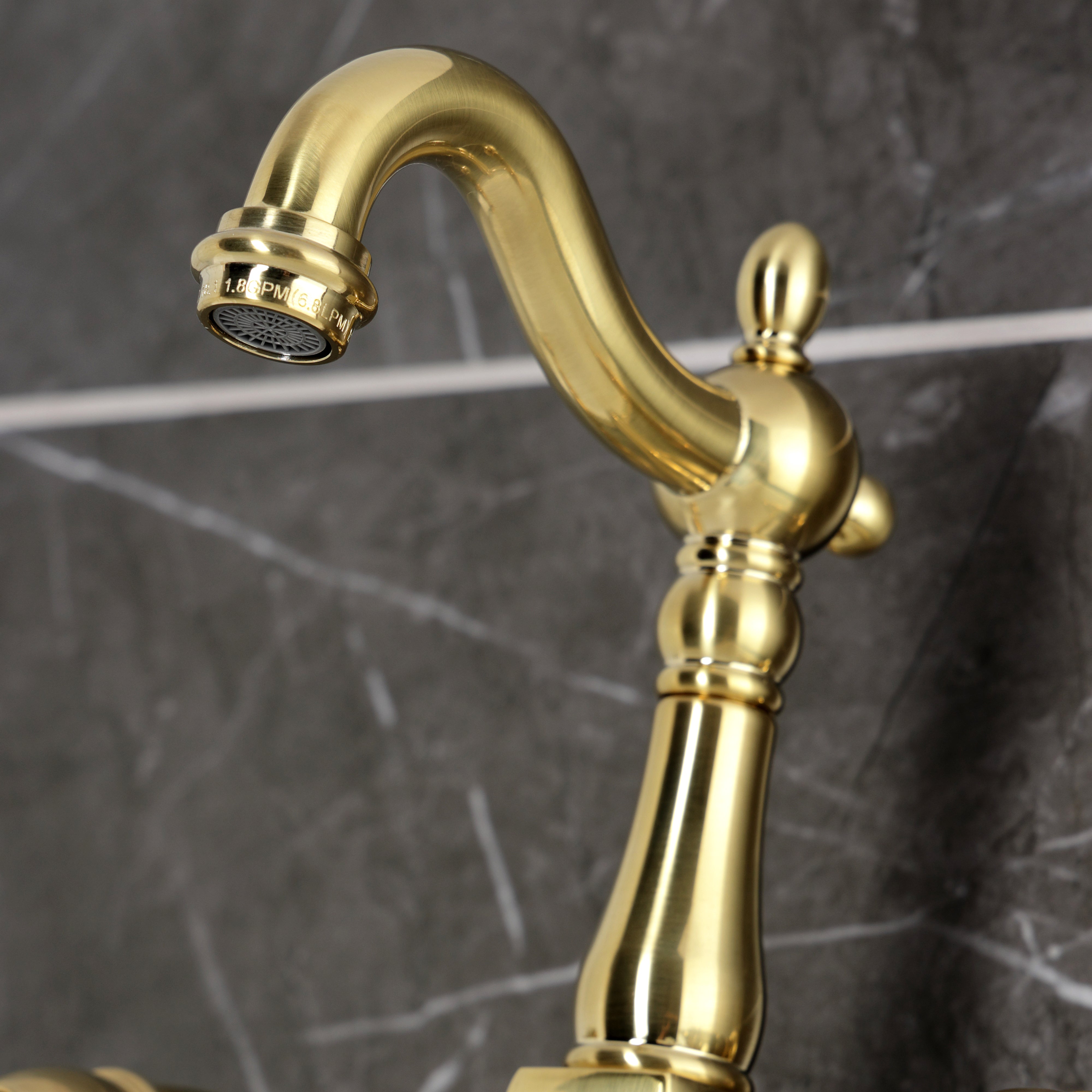 Kingston KS2443AX Heritage Two-Handle Wall Mount Bridge Kitchen Faucet, Antique Brass spout detail on marble background