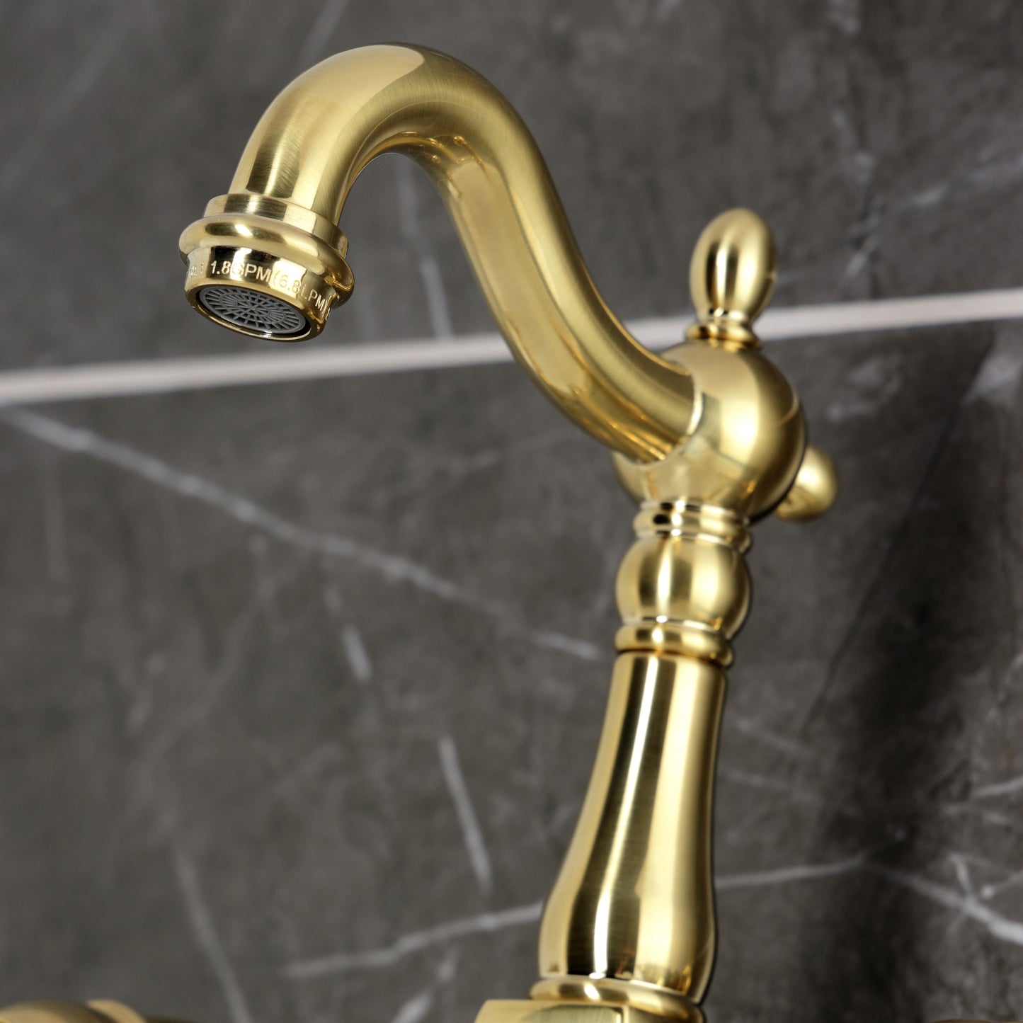 Kingston KS2443AX Heritage Two-Handle Wall Mount Bridge Kitchen Faucet, Antique Brass spout detail on marble background