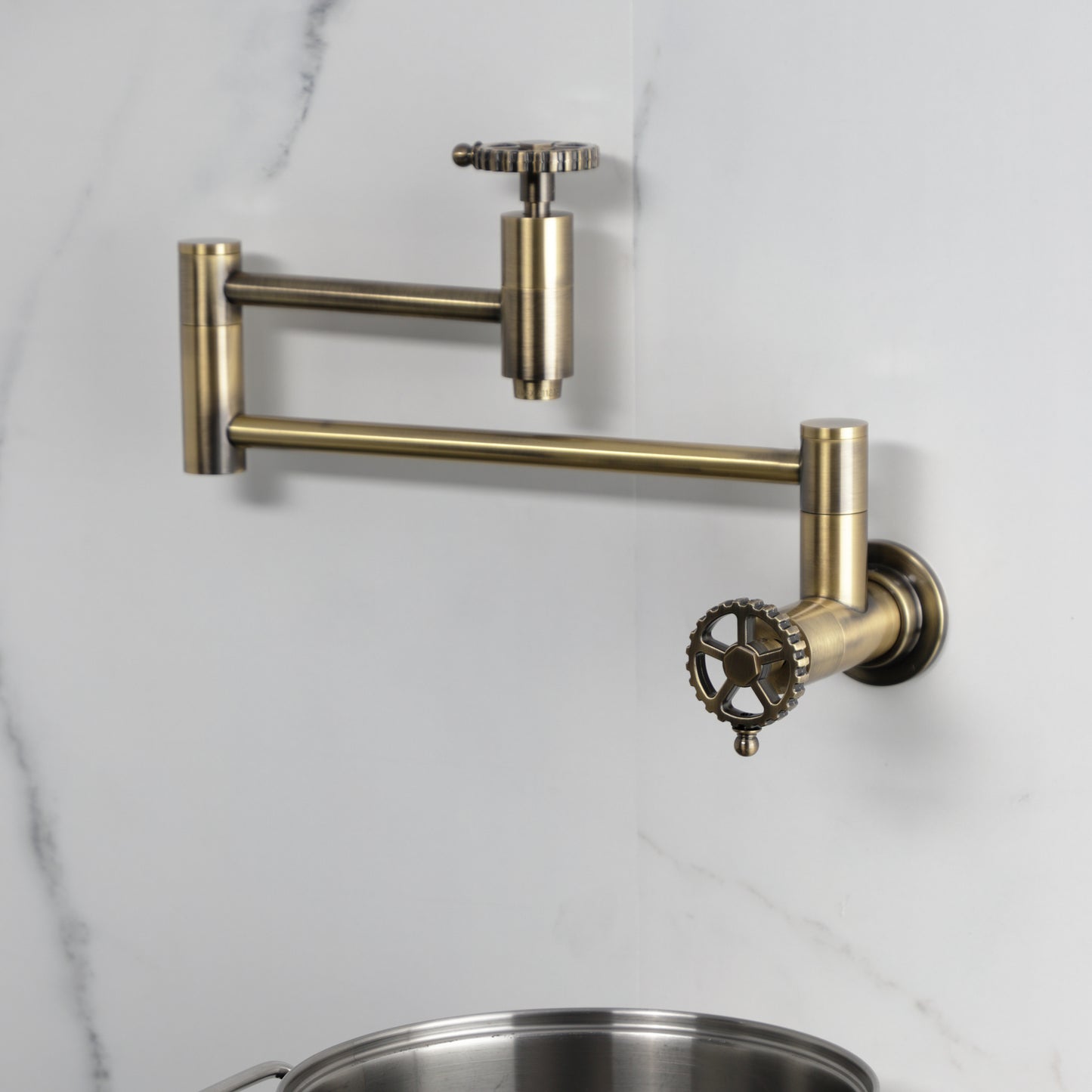 Kingston Brass KS8103CG Fuller Wall Mount Pot Filler Faucet, Antique Brass mounted on a wall with pot below.