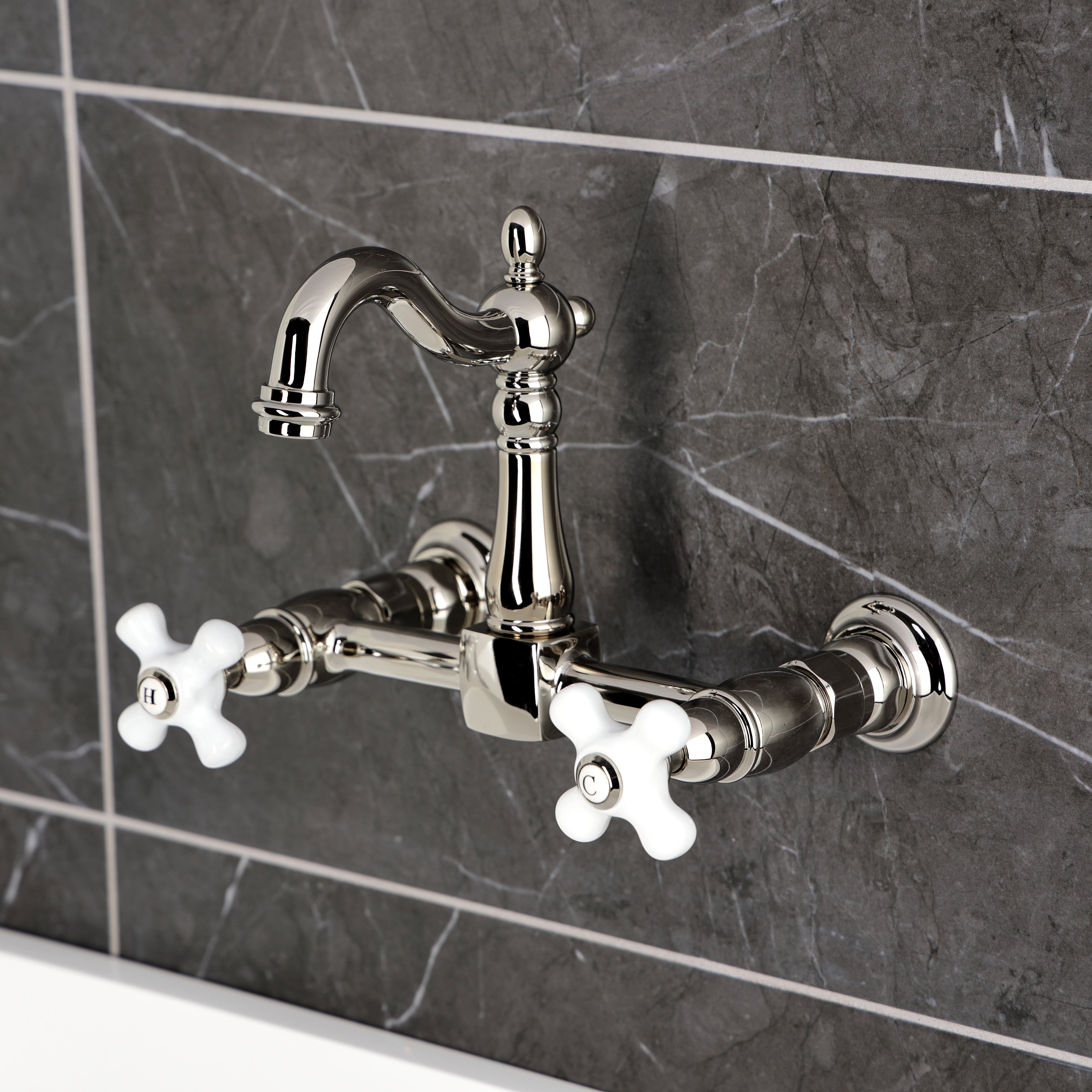 Kingston KS2443PX Heritage Two-Handle Wall Mount Bridge Kitchen Faucet, Antique Brass with white porcelain cross handles.