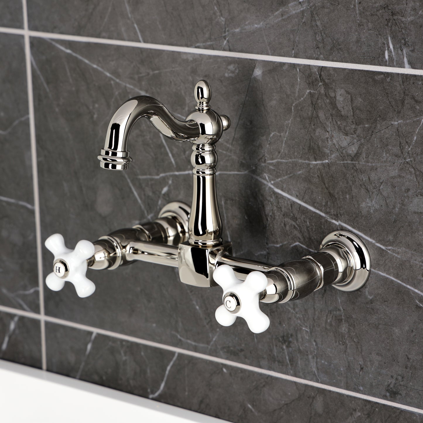 Kingston KS2443PX Heritage Two-Handle Wall Mount Bridge Kitchen Faucet, Antique Brass with white porcelain cross handles.