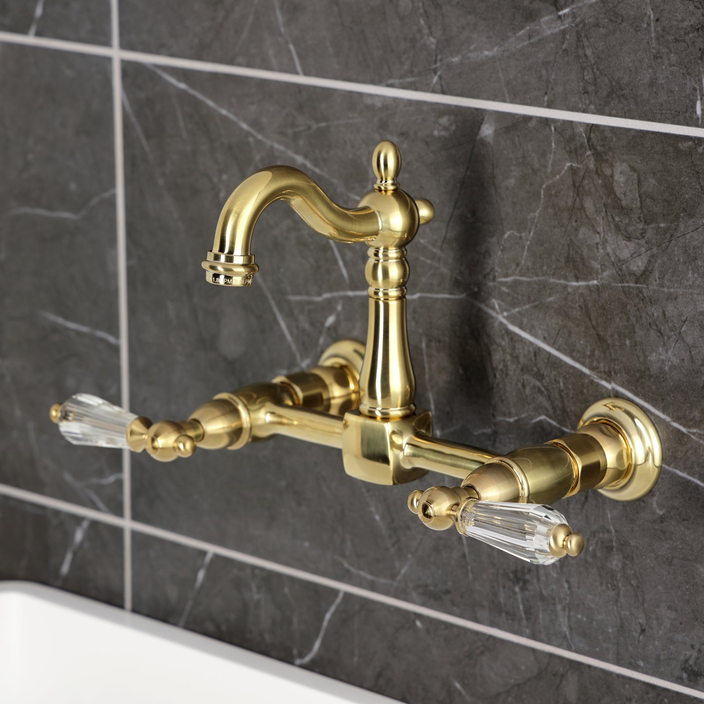Kingston KS2443WLL Willshire Two-Handle Wall Mount Bridge Kitchen Faucet, Antique Brass on a dark marble wall.