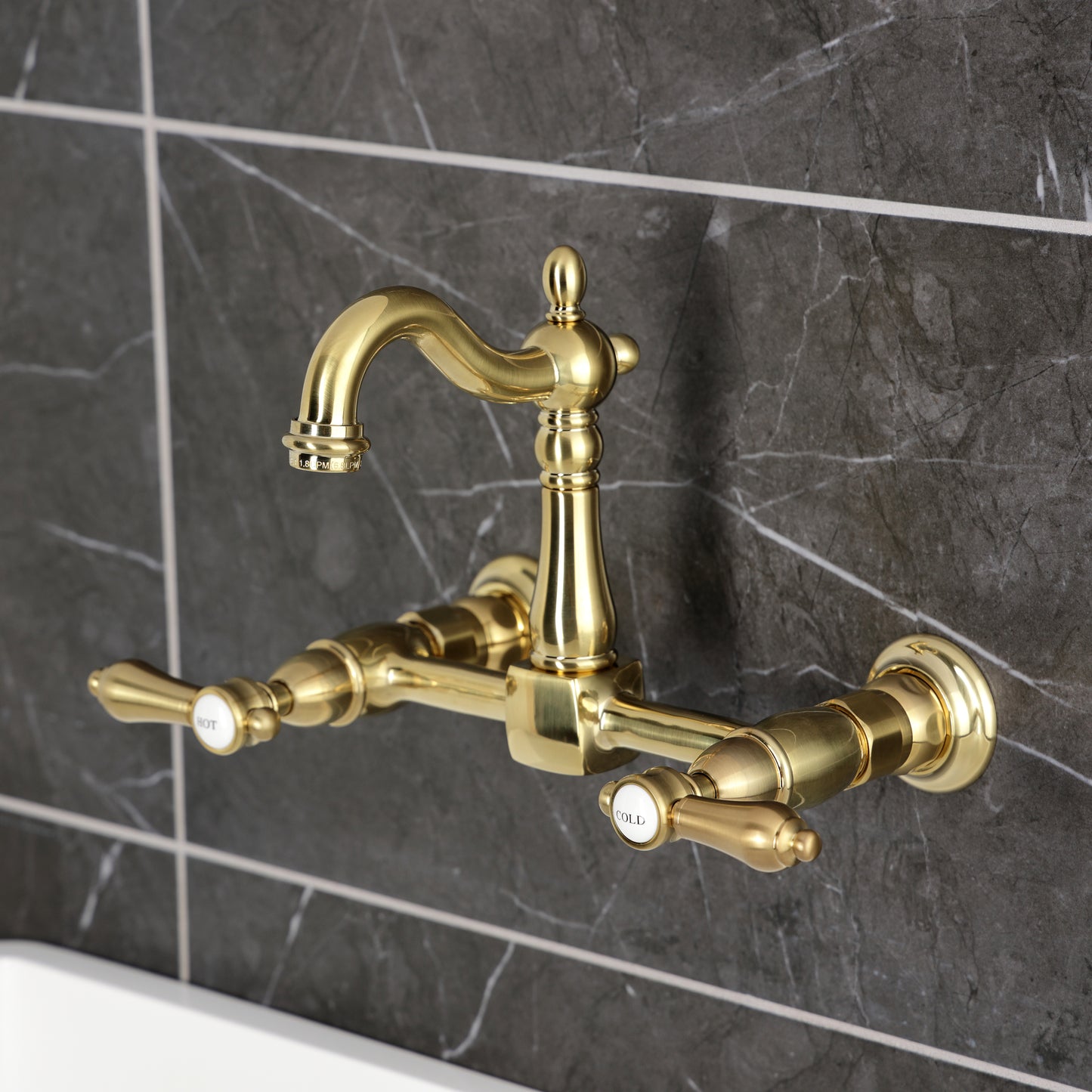 Kingston KS2443BAL Heirloom Two-Handle Wall Mount Bridge Kitchen Faucet, Antique Brass on a gray tile background.
