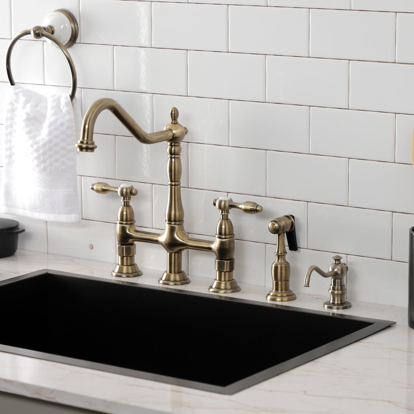 Kingston KS1273TALBS Tudor Bridge Kitchen Faucet with Brass Sprayer, Antique Brass installed in a modern kitchen setting.