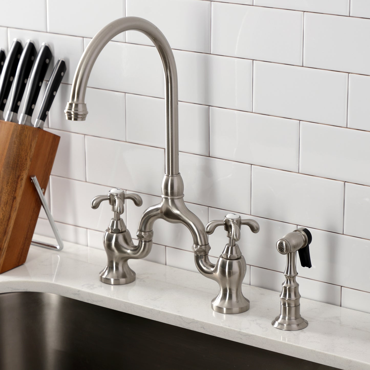Kingston KS7793TXBS French Country Bridge Kitchen Faucet with Brass Sprayer, Antique Brass in a modern kitchen setting.