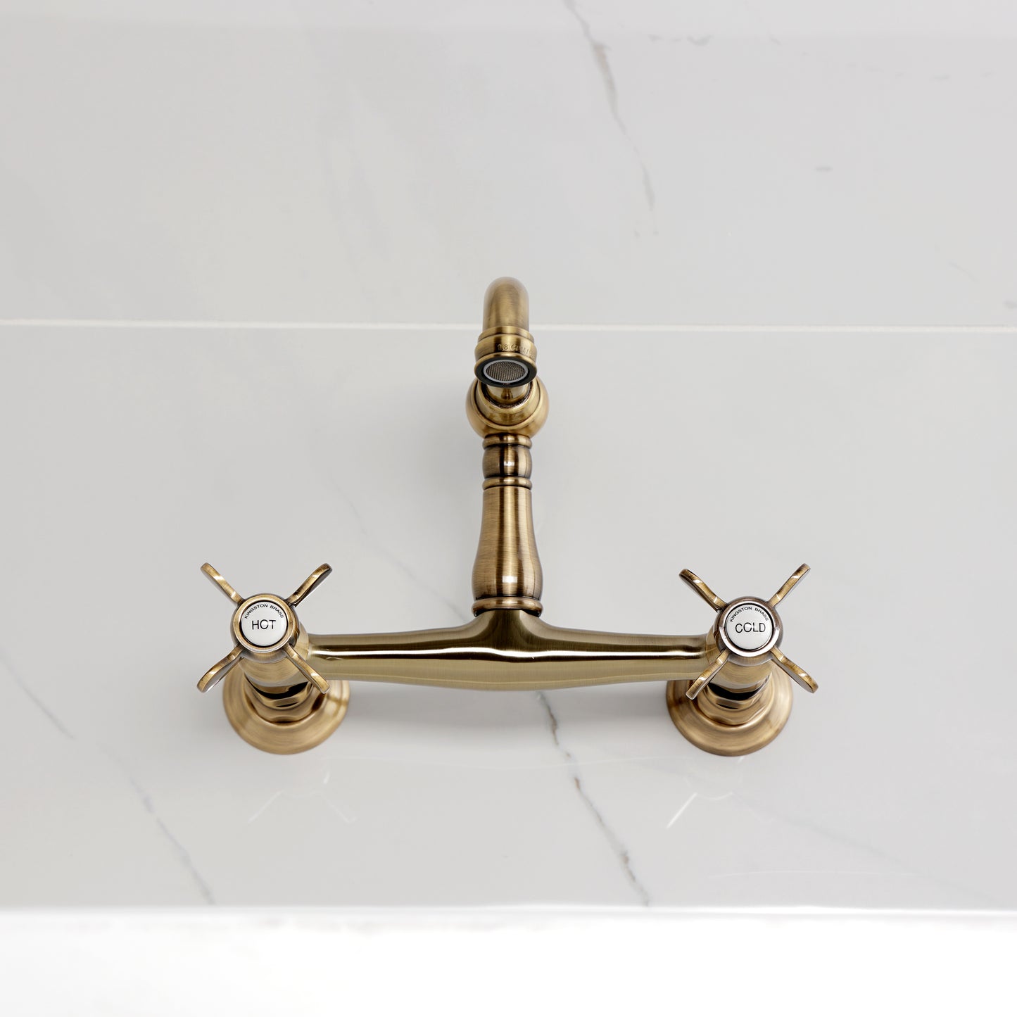 Kingston KS3253BEX Essex Two-Handle Wall Mount Bridge Kitchen Faucet, Antique Brass on a marble countertop.