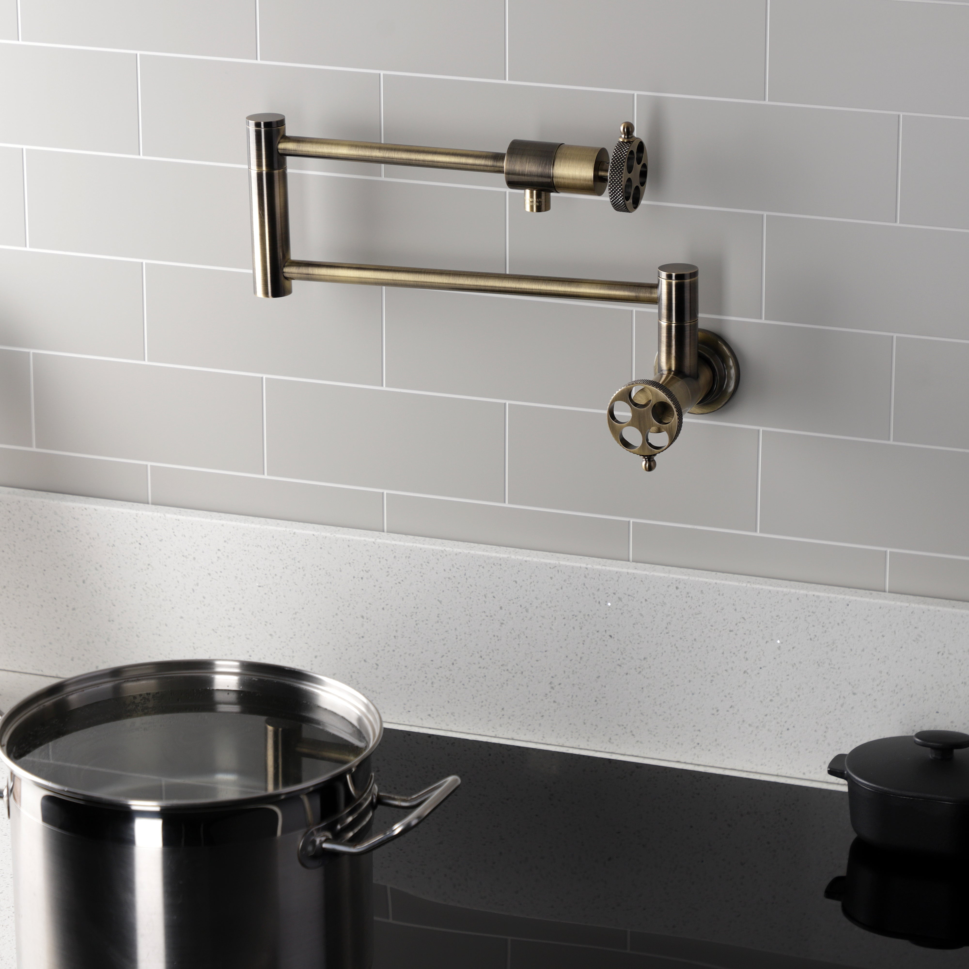 Kingston Brass KS4103RKX Webb Wall Mount Pot Filler Faucet with Knurled Handle, Antique Brass on a modern kitchen backsplash.