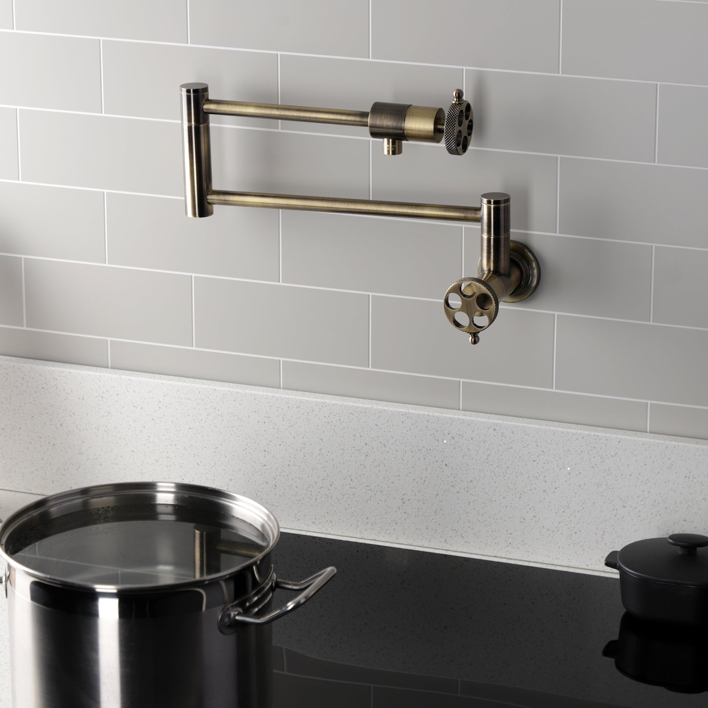 Kingston Brass KS4103RKX Webb Wall Mount Pot Filler Faucet with Knurled Handle, Antique Brass on a modern kitchen backsplash.