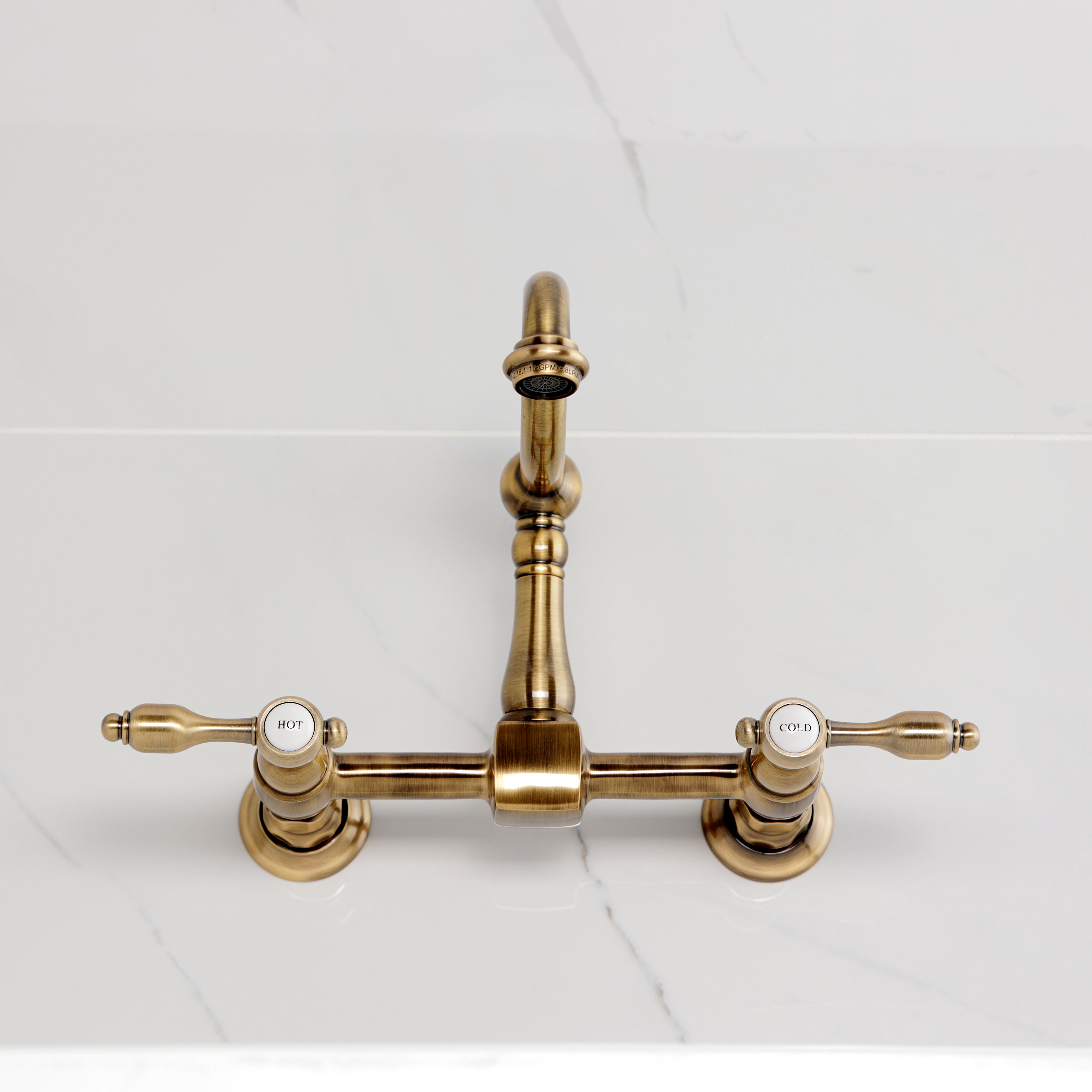 Kingston KS1263TAL Tudor Two-Handle Wall Mount Bridge Kitchen Faucet, Antique Brass on white countertop.