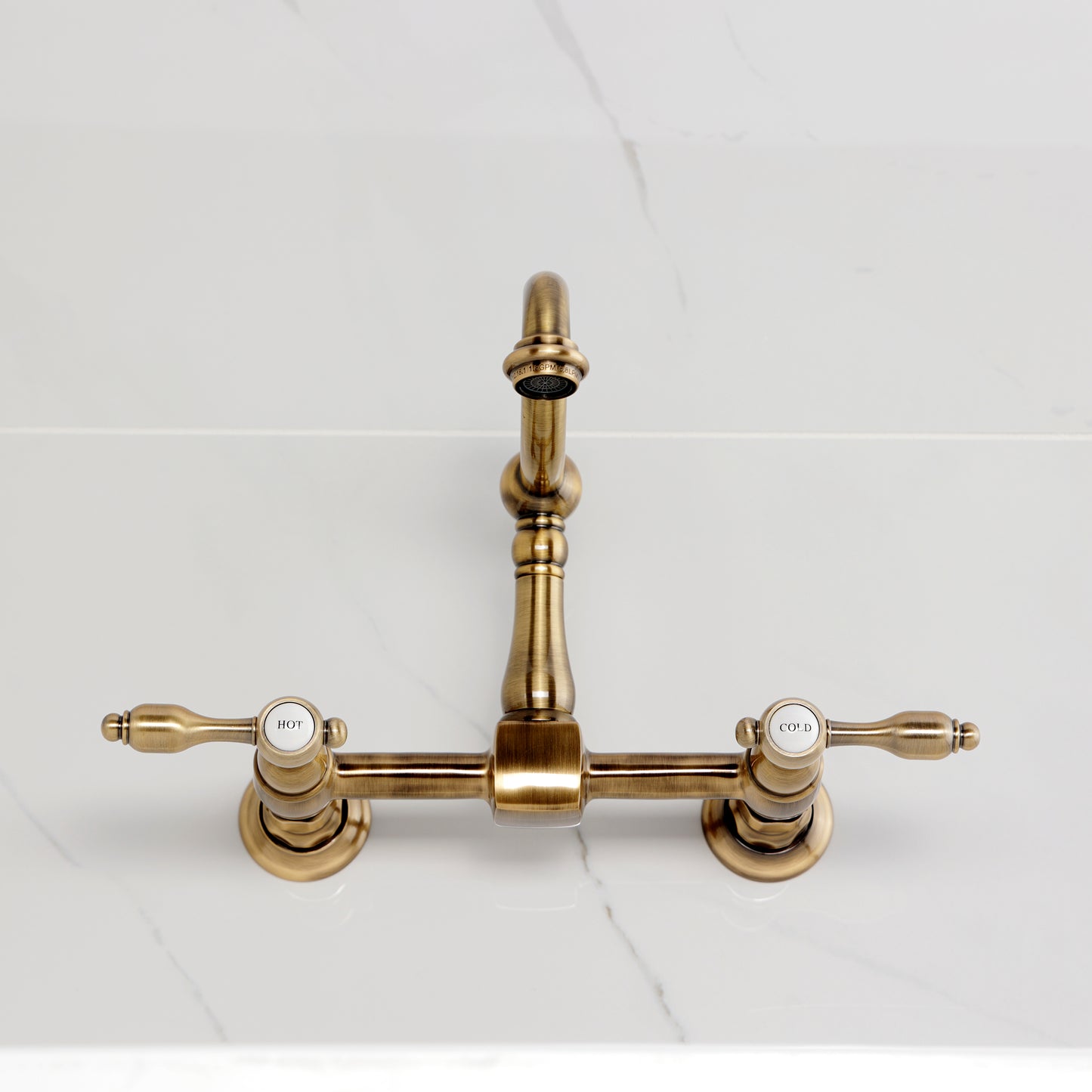 Kingston KS1263TAL Tudor Two-Handle Wall Mount Bridge Kitchen Faucet, Antique Brass on white countertop.
