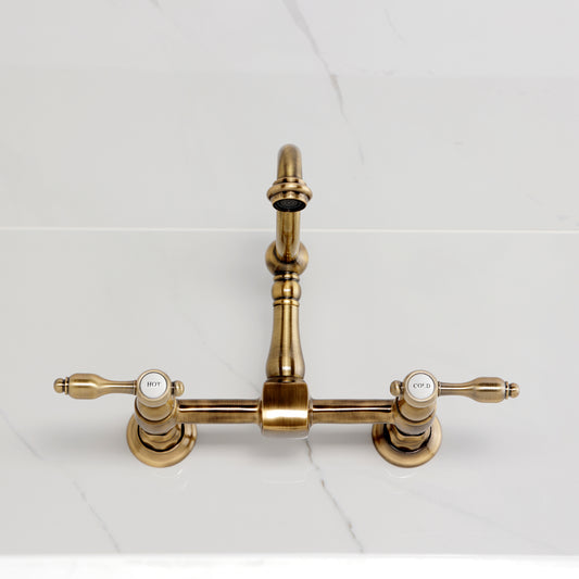 Kingston KS1263TAL Tudor Two-Handle Wall Mount Bridge Kitchen Faucet, Antique Brass on white countertop.
