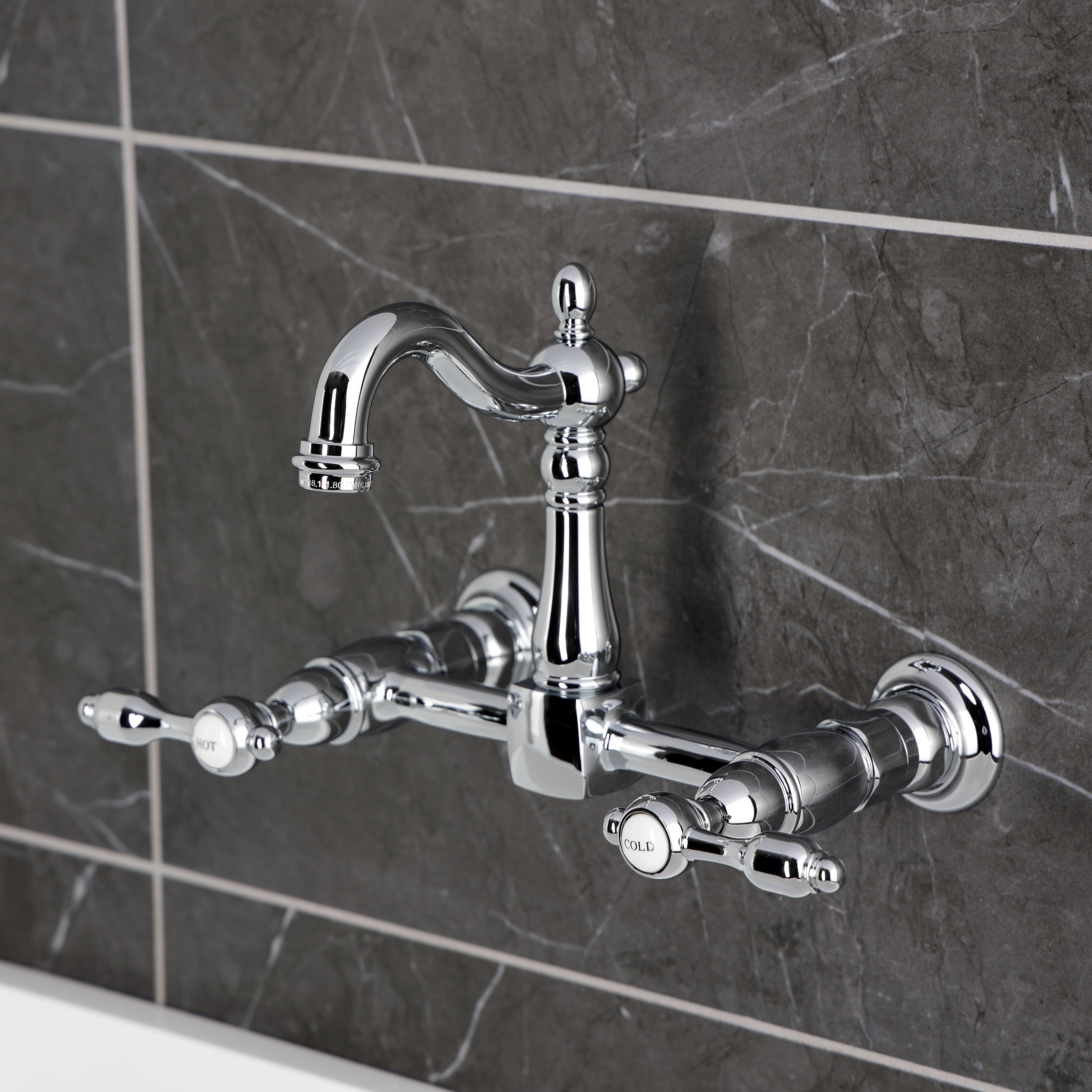 Kingston KS2443TAL Tudor Two-Handle Wall Mount Bridge Kitchen Faucet, Antique Brass in chrome finish against gray tile.