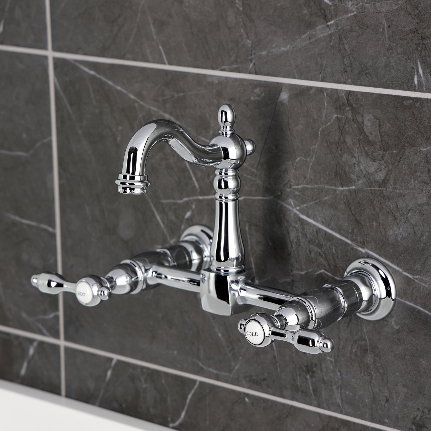 Kingston KS2443TAL Tudor Two-Handle Wall Mount Bridge Kitchen Faucet, Antique Brass in chrome finish against gray tile.