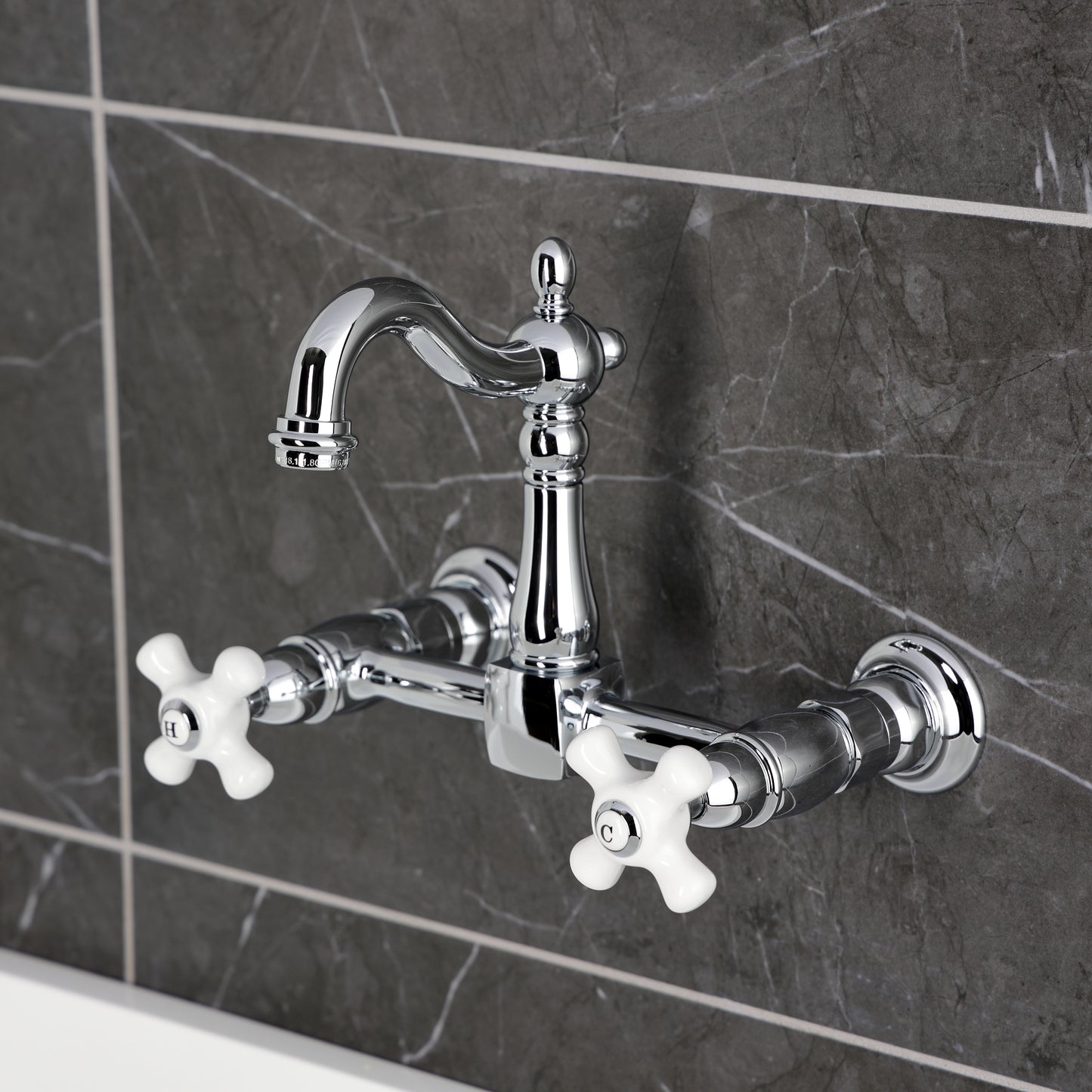 Kingston KS2443PX Heritage Two-Handle Wall Mount Bridge Kitchen Faucet, Antique Brass on a dark tiled wall.