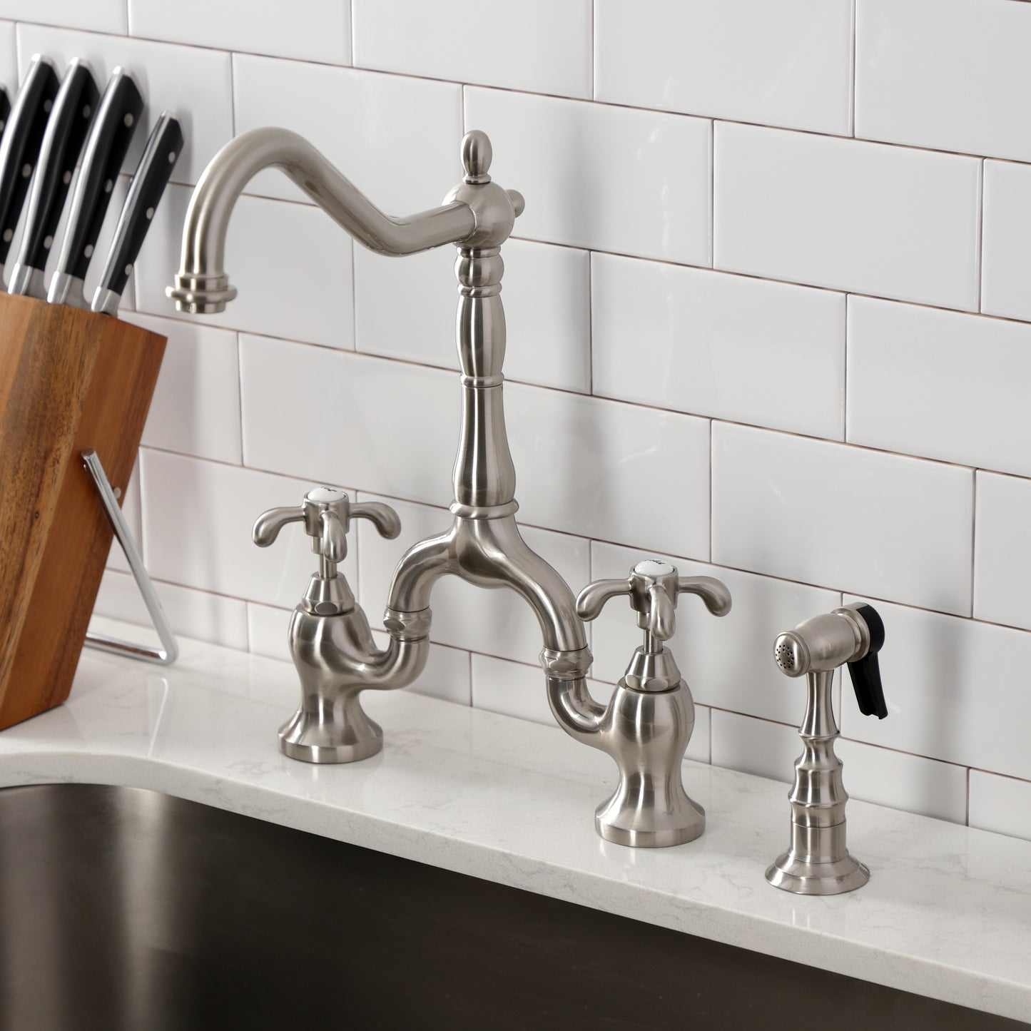Kingston KS7753TXBS French Country Bridge Kitchen Faucet with Brass Sprayer, Antique Brass displayed in kitchen setting.