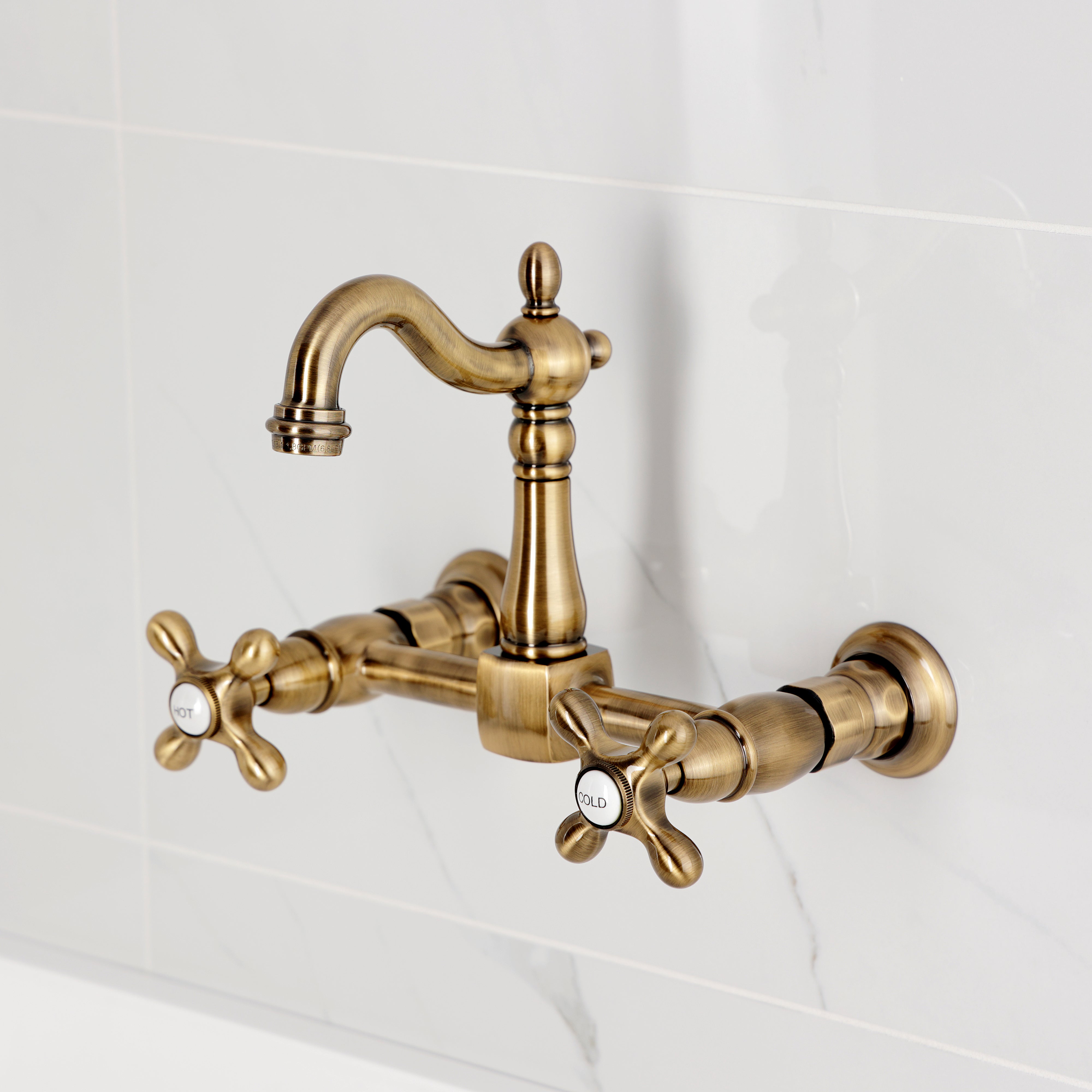 Kingston KS2443AX Heritage Two-Handle Wall Mount Bridge Kitchen Faucet, Antique Brass on a marble background