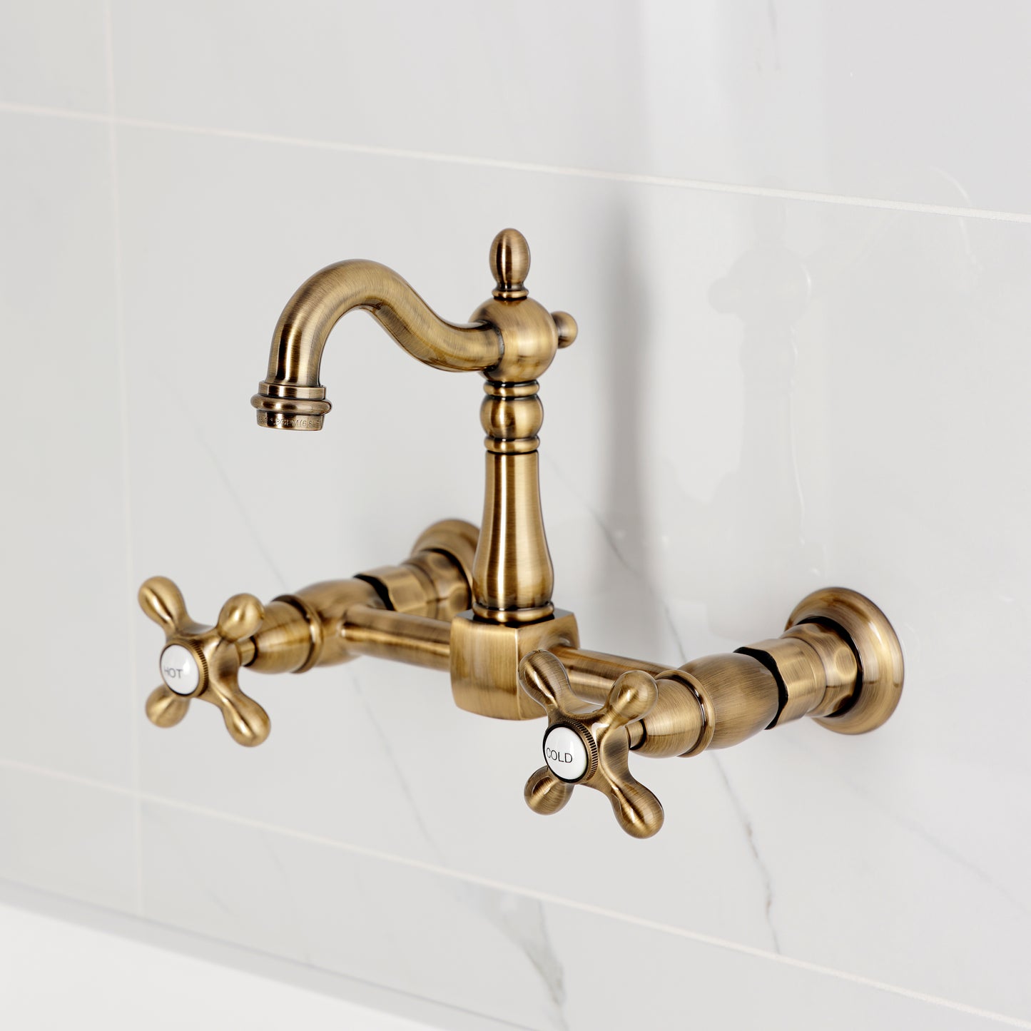Kingston KS2443AX Heritage Two-Handle Wall Mount Bridge Kitchen Faucet, Antique Brass on a marble background