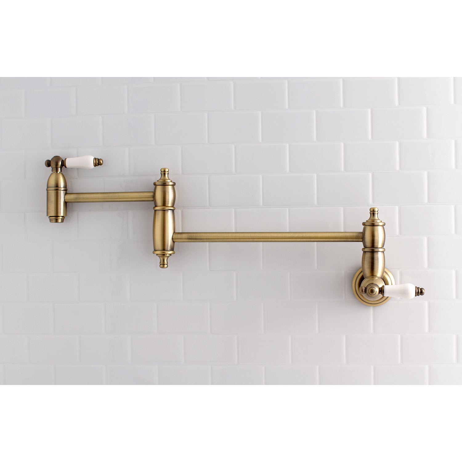 Kingston Brass KS3103PL Restoration Wall Mount Pot Filler Faucet, Antique Brass on a white tiled wall.